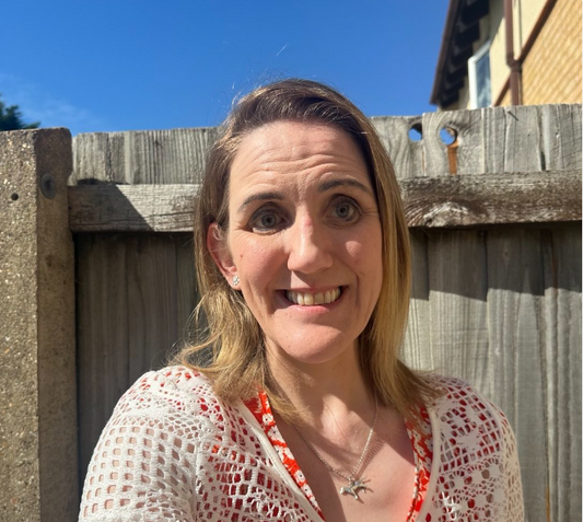 Siobhan, a white female with light brown hair stood outside with a blue sky in the background, she is smiling at the camera