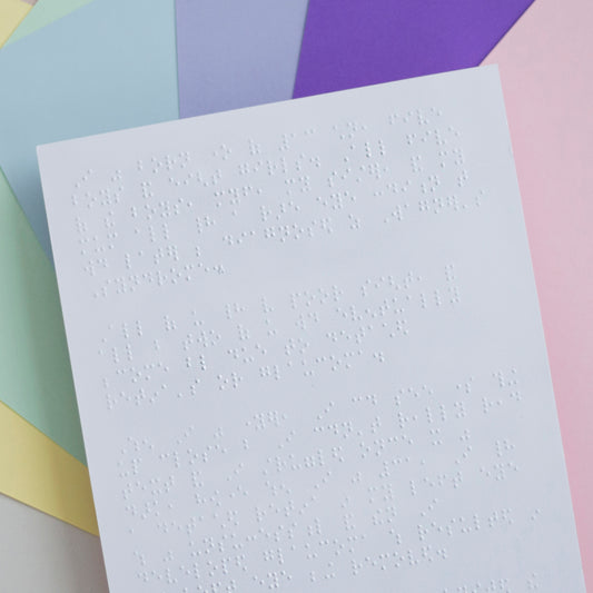 Sheets of coloured paper, the top sheet is white and has braille on.