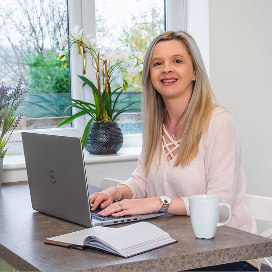 Hayley Kellard, a blonde woman sat at a laptop, smiling towards the camera