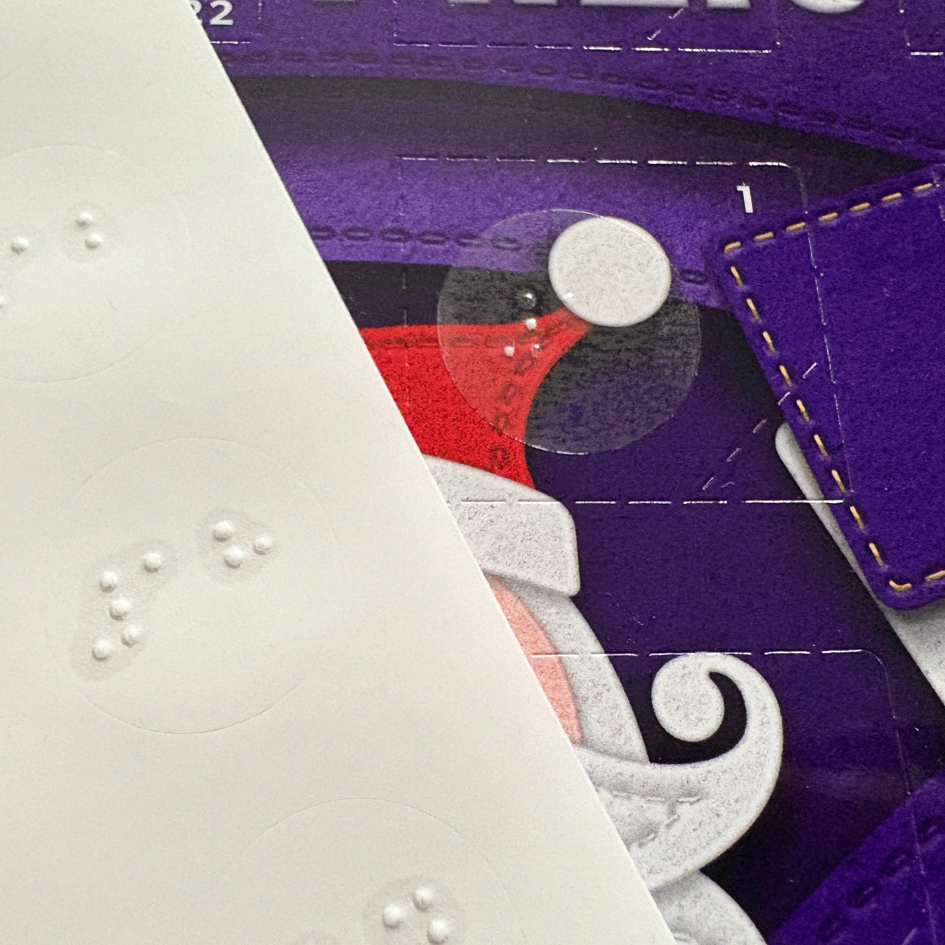 A close up of an advent calendar showing the number 1 door with a braille sticker. A sheet of braille stickers is also visible.