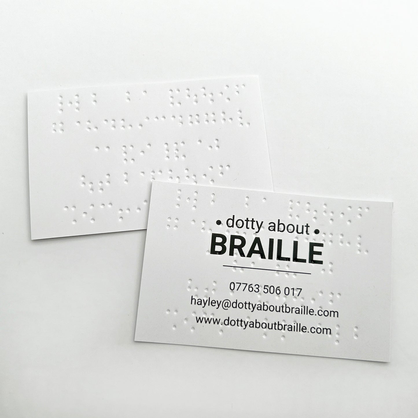 Two Dotty About Braille business cards, showing how the braille shows through when printed on the other side.