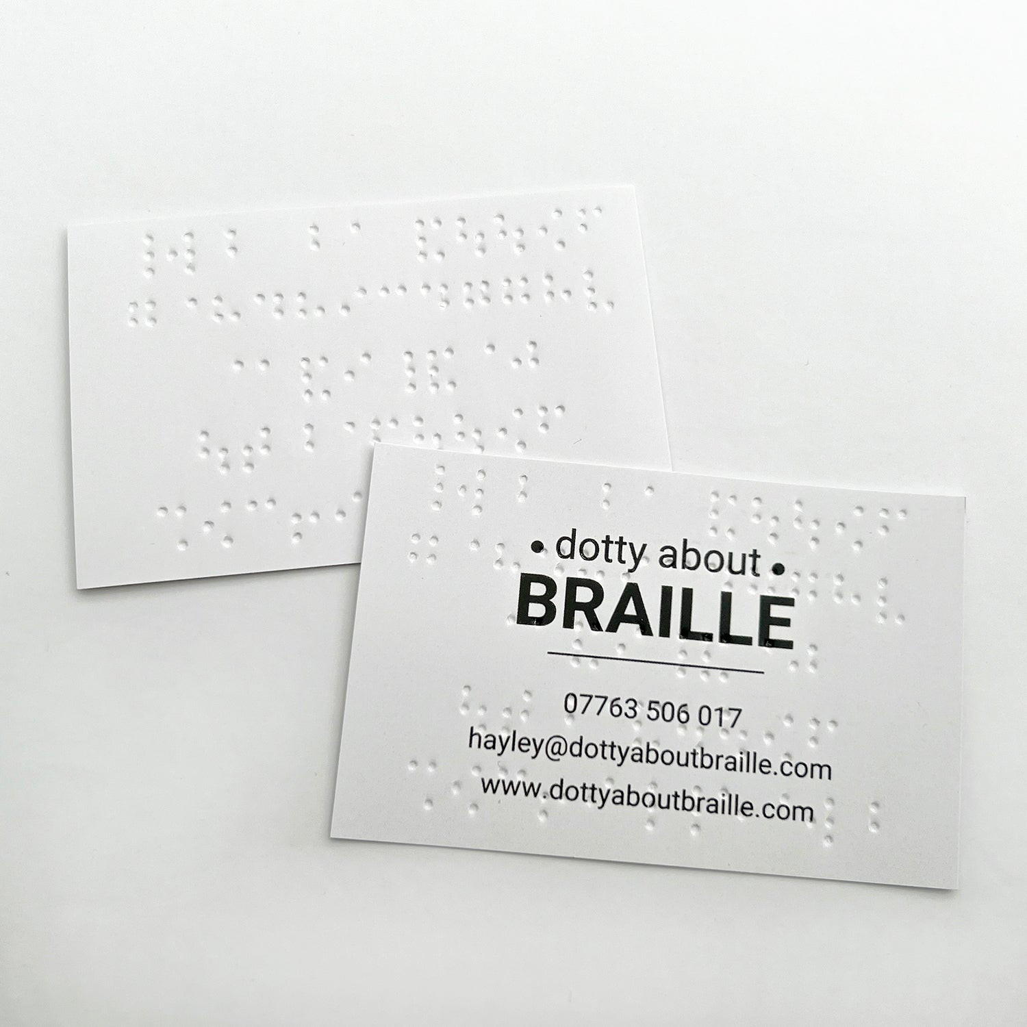 Two Dotty About Braille business cards, showing how the braille shows through when printed on the other side.