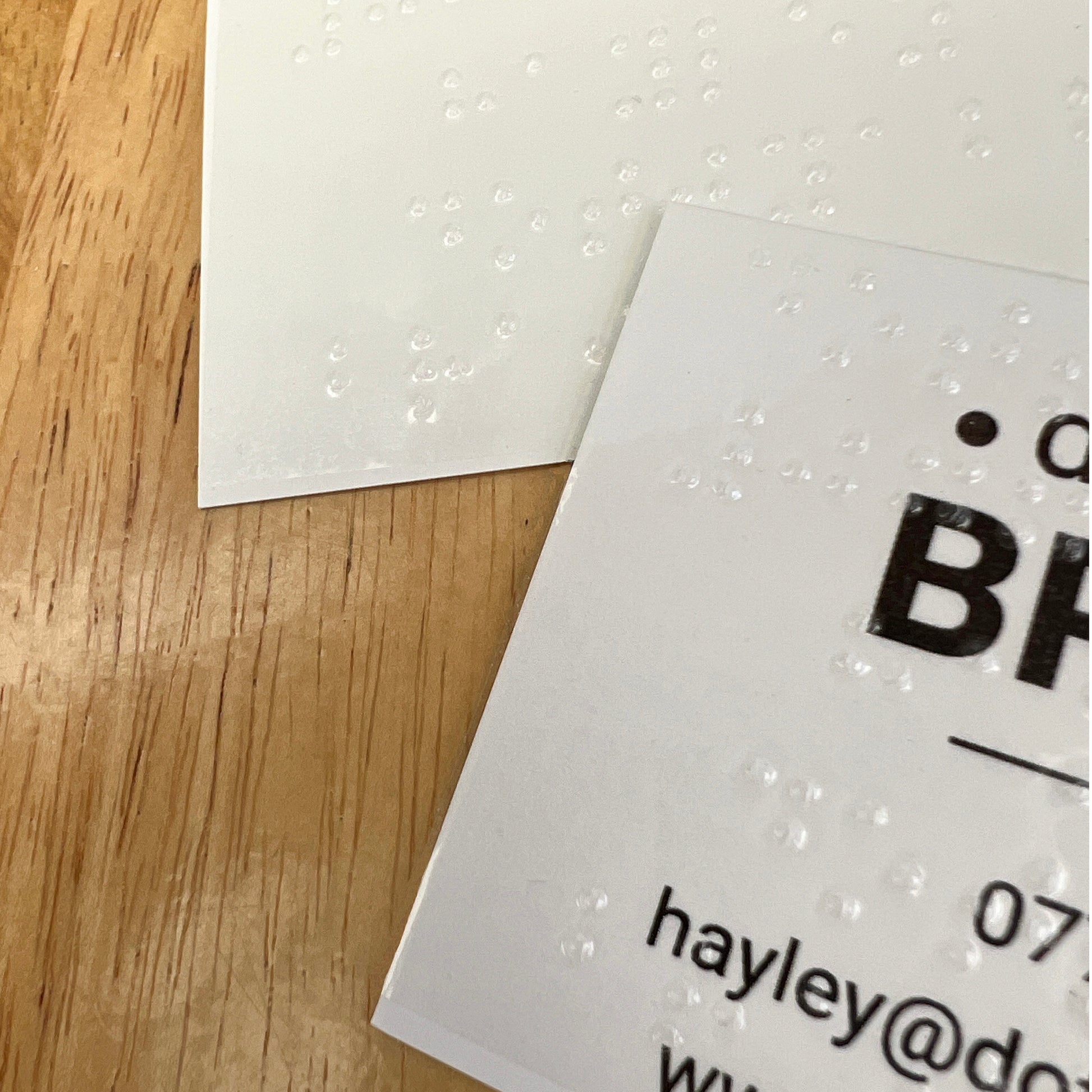 A close up of a blank business card and printed dotty about braille card, both have braille labels stuck on them.
