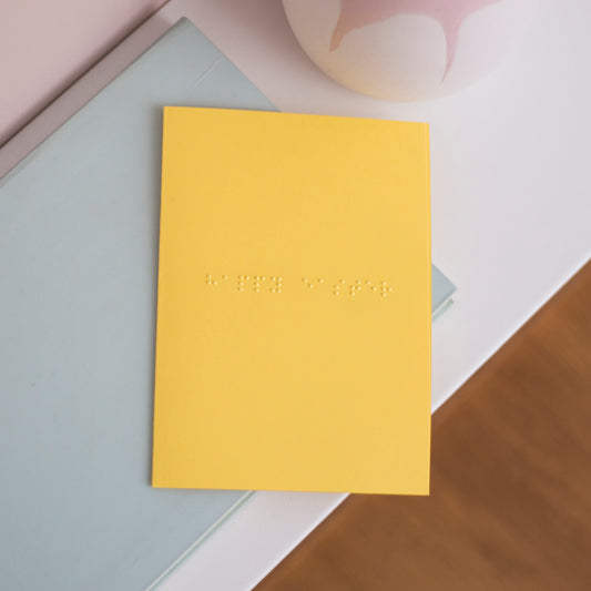 A vibrant yellow card with happy easter written in lower case braille.