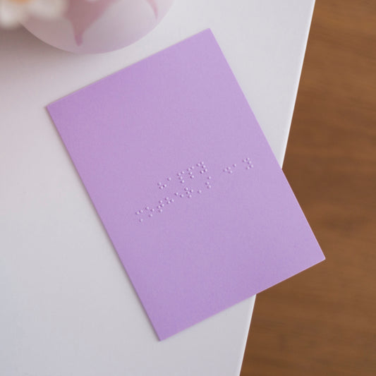 A pastel purple card with Happy Mother's Day written in lower case braille.
