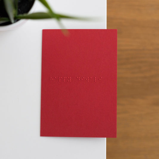 A vibrant red card lay flat on a table with happy diwali written in lower case grade one braille.