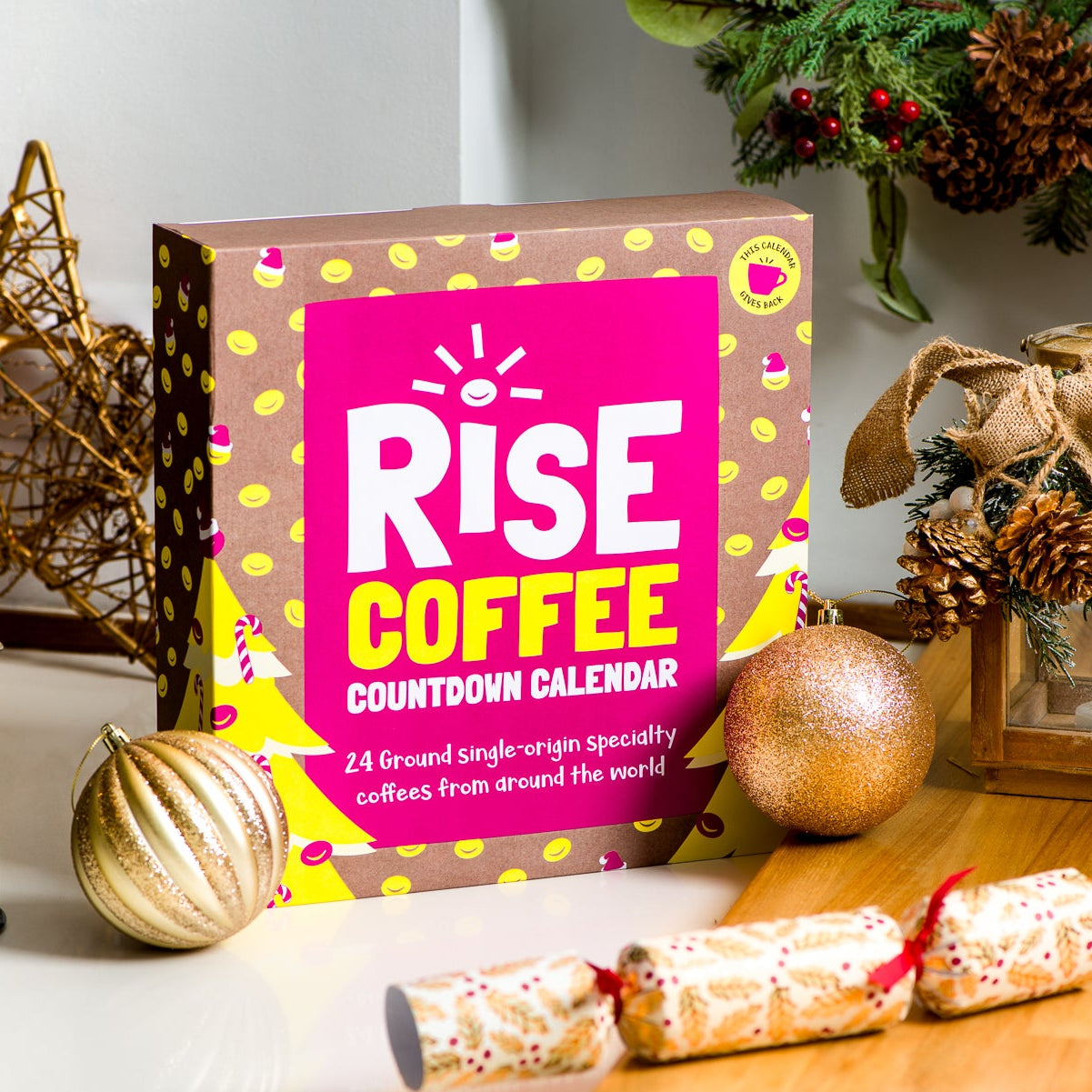 RISE Coffee Advent Calendar surrounded by festive decorations, including baubles, a Christmas cracker, and a cafetière on a wooden surface.