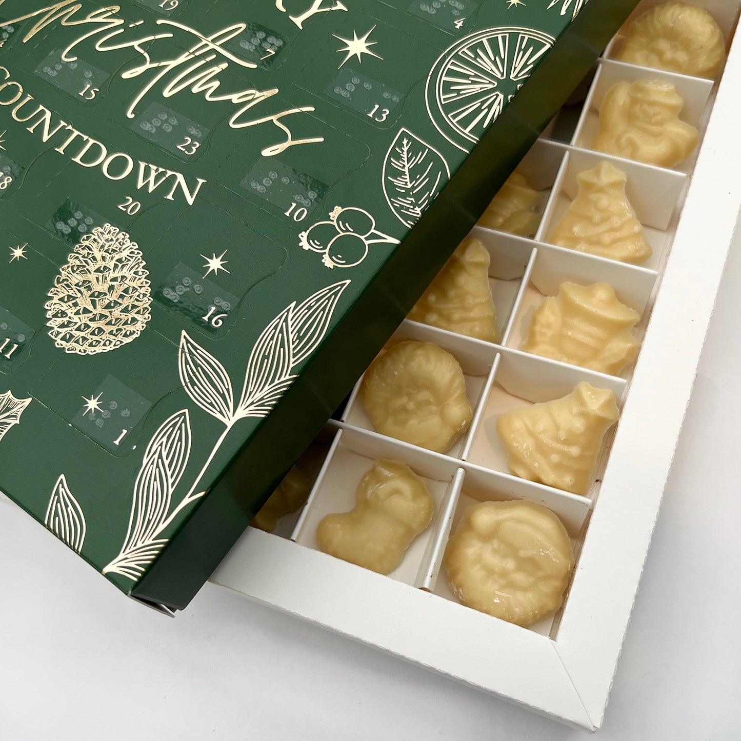 A close up shot of the inside of the advent calendar, showing multiple pieces of white chocolate. The green advent calendar box is sat on top, at an angle.