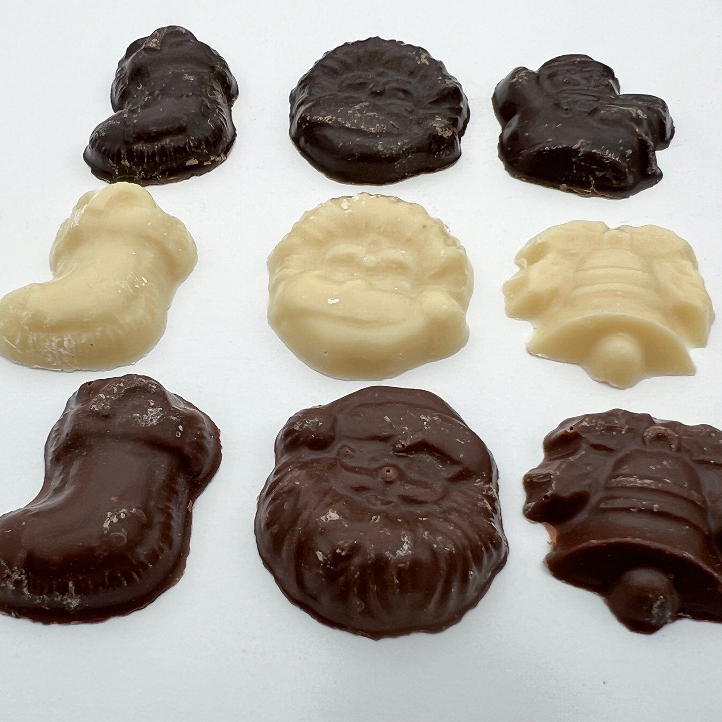 A close up of nine pieces of chocolate in various Christmas themed shapes such as a bell, santa and a stocking. The chocolate is a mix of white, dark and milk.