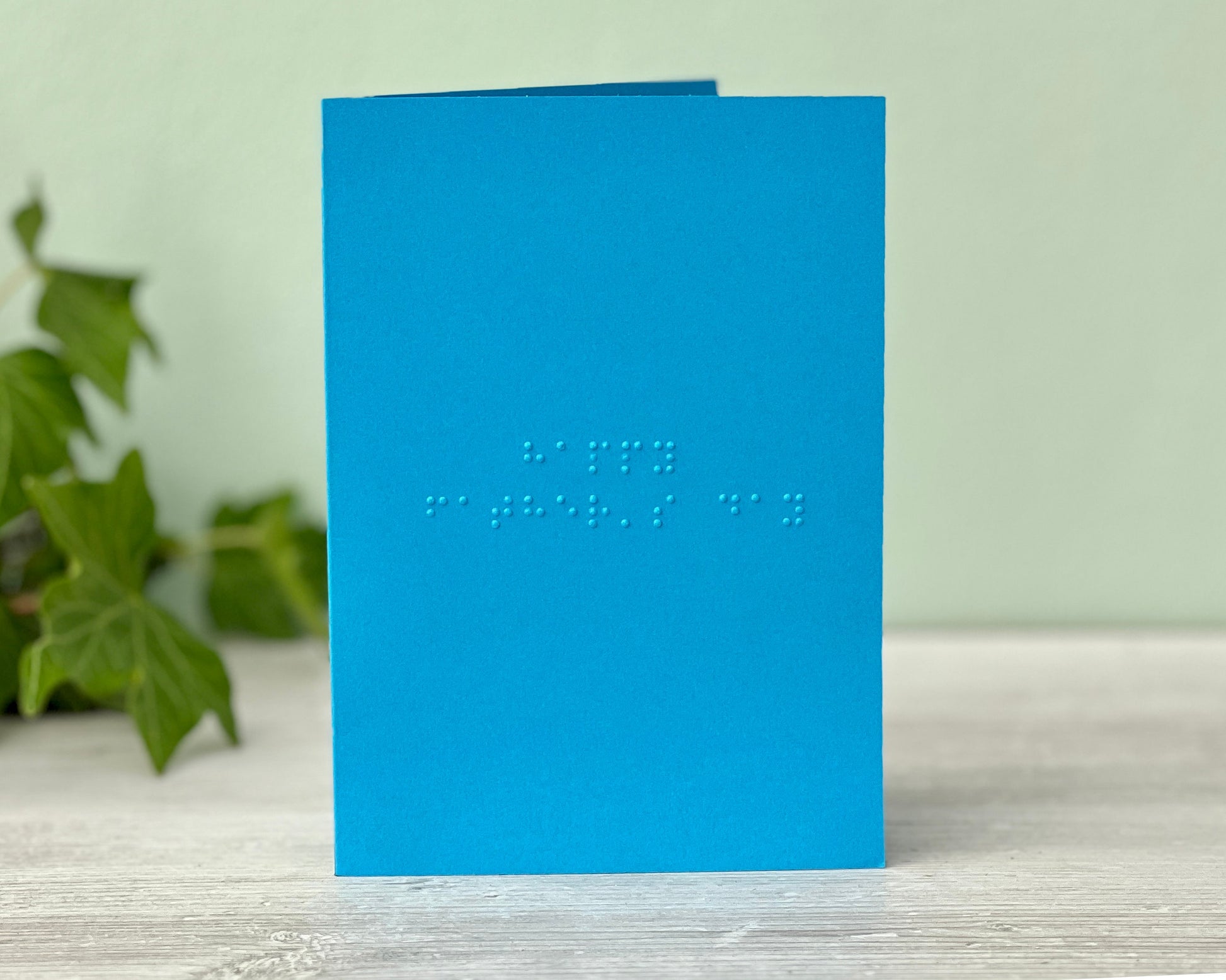 A vibrant blue landscape greetings card with happy father's day written in grade 1 lower case braille.