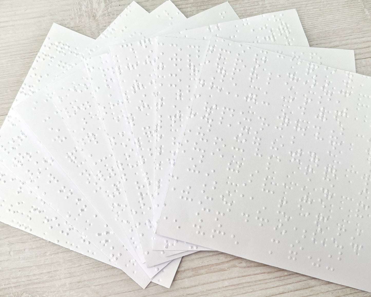 A close up of eight sheets of 11x1.5cm white braille paper.