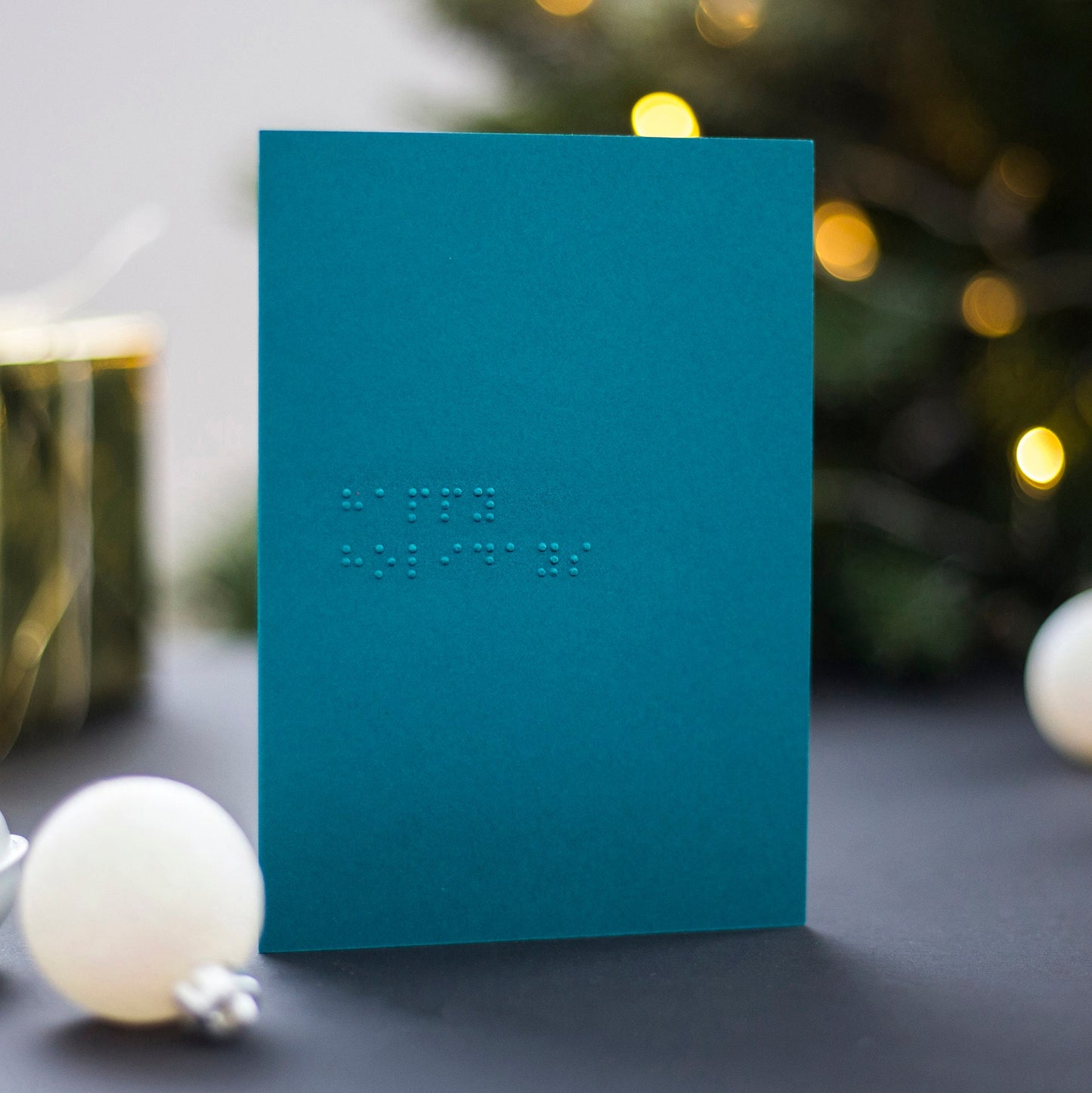 A teal braille Christmas card with happy holidays written in lower case UEB.