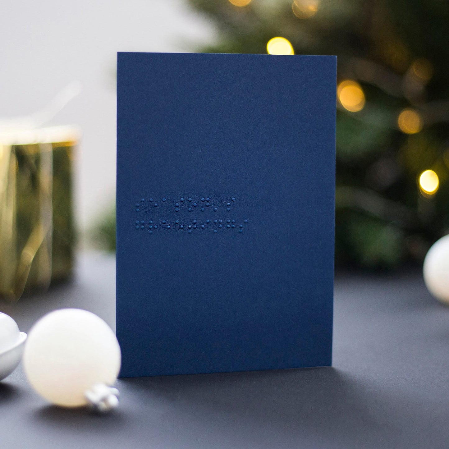 A navy blue braille Christmas card with season's greetings written in lower case UEB.