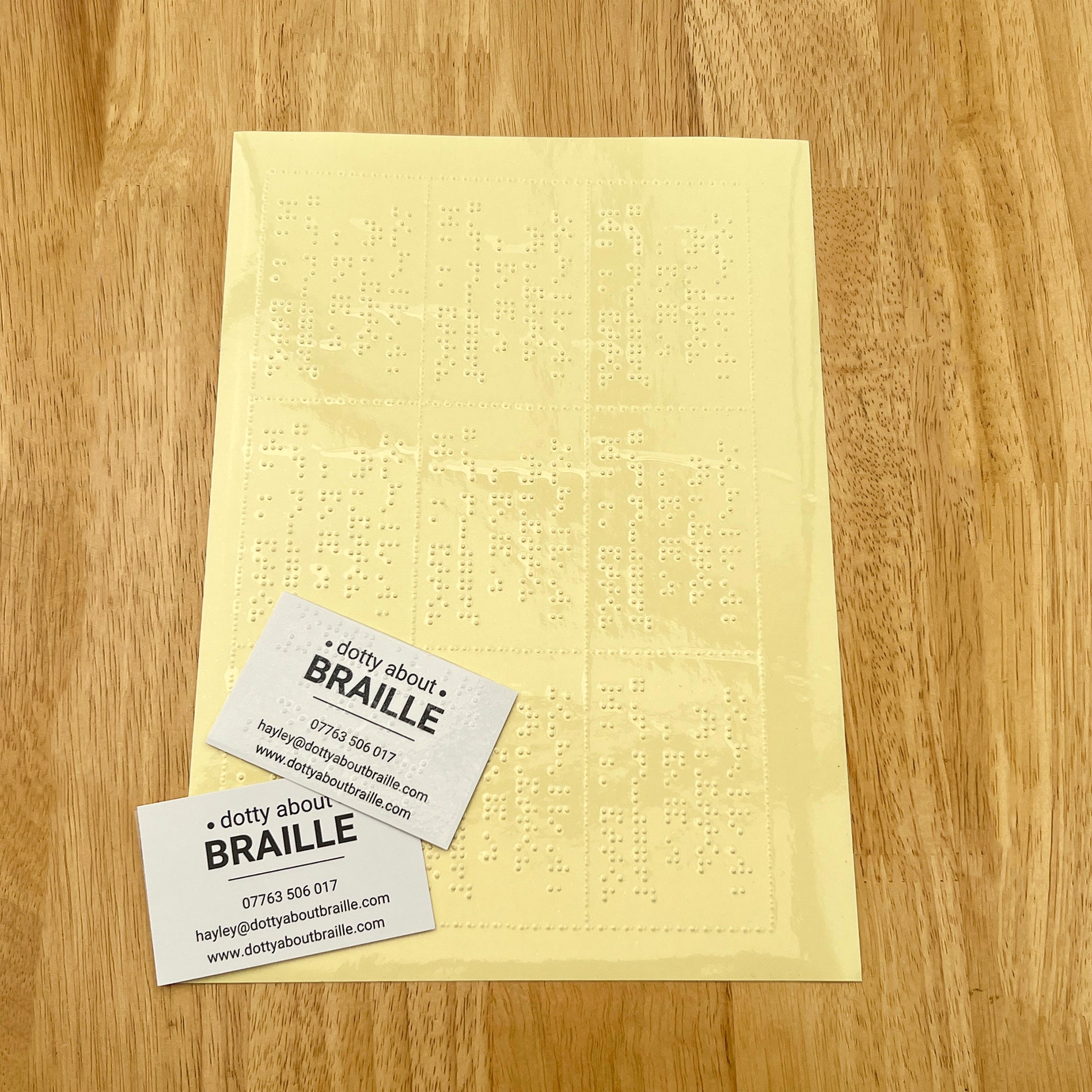 A4 sheet of clear braille labels on yellow backing paper with two dotty about braille business cards in the bottom left corner.