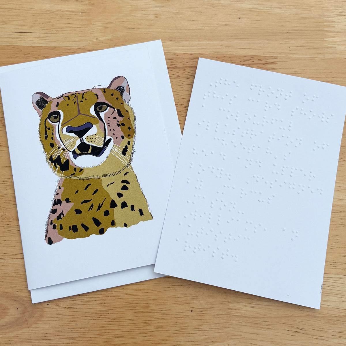 A greetings card showing a colourful illustration of a cheetah's head and upper body against a white background. There is a white braille note at the side.