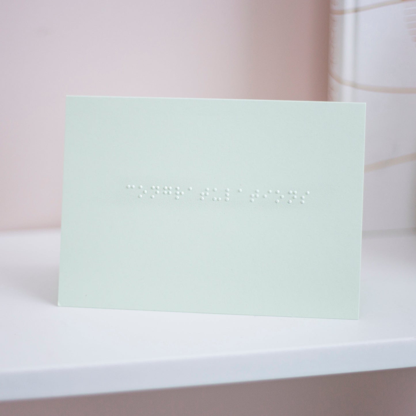 A pastel green card with congratulations written in lower case braille.