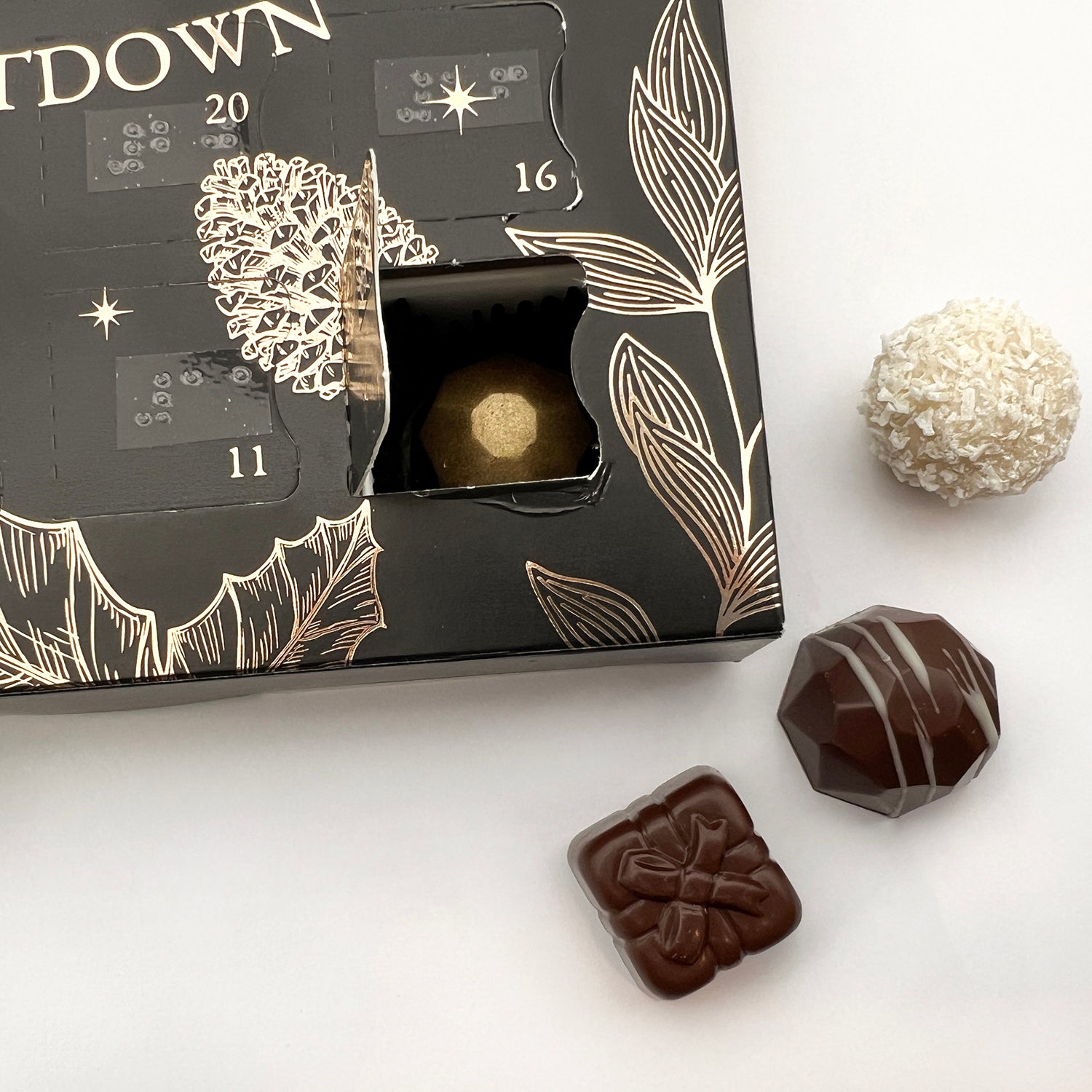 A close up of the advent calendar with one of the doors open a gold chocolate visible behind the door, there are three chocolates next to the box.