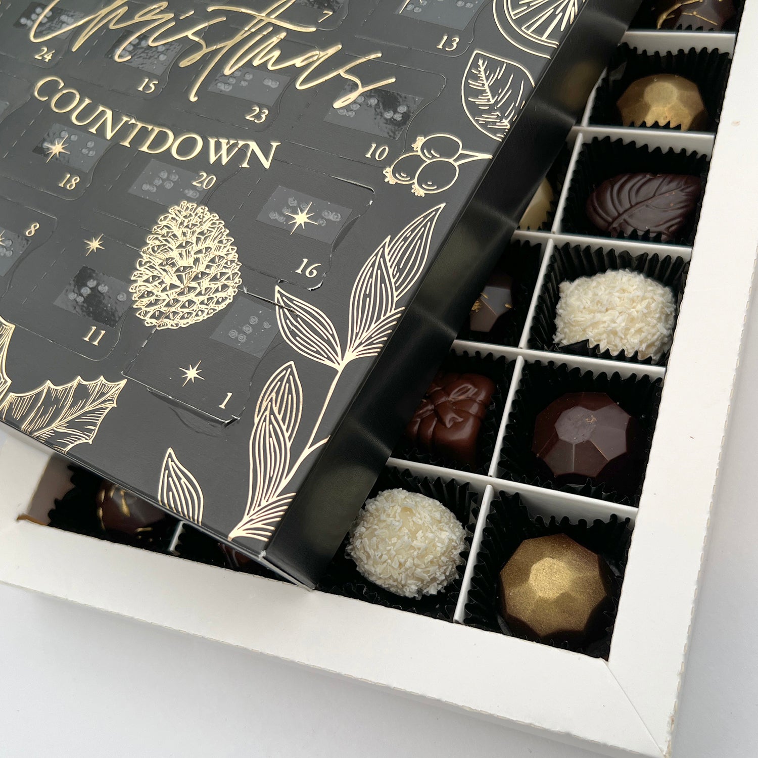 A close up shot of the inside of the advent calendar, showing handcrafted luxury chocolates. The black advent calendar box is sat on top, at an angle.
