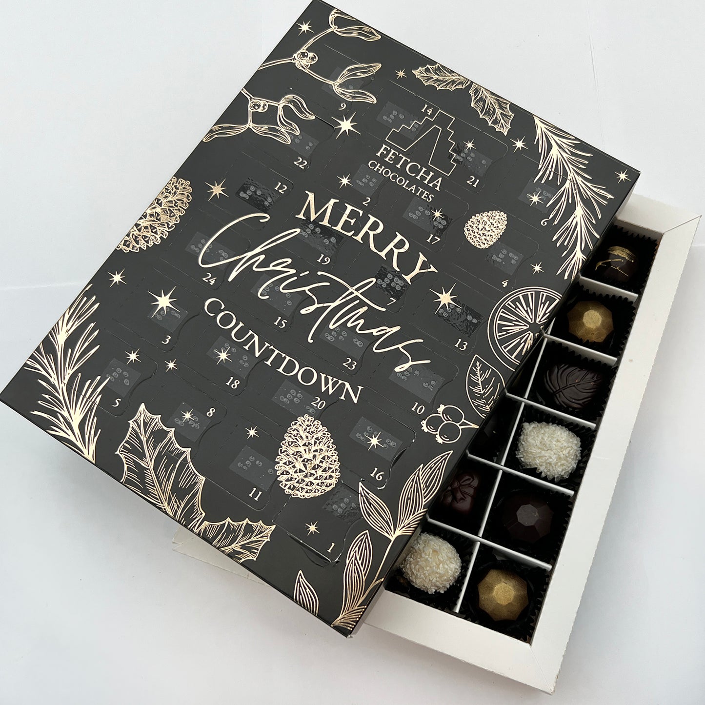 A shot of the inside of the advent calendar, showing handcrafted luxury chocolates. The black advent calendar box is sat on top, at an angle.