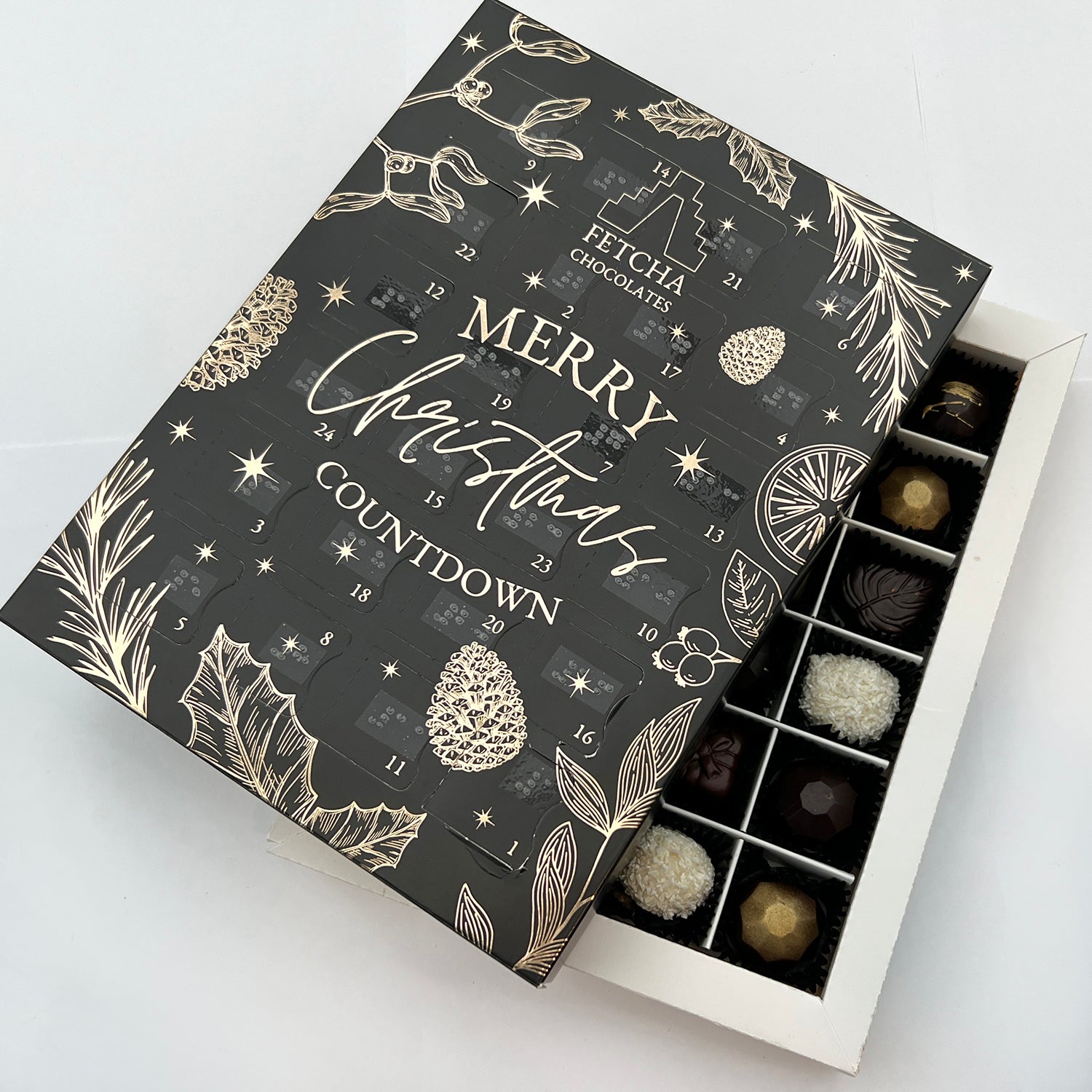 A shot of the inside of the advent calendar, showing handcrafted luxury chocolates. The black advent calendar box is sat on top, at an angle.