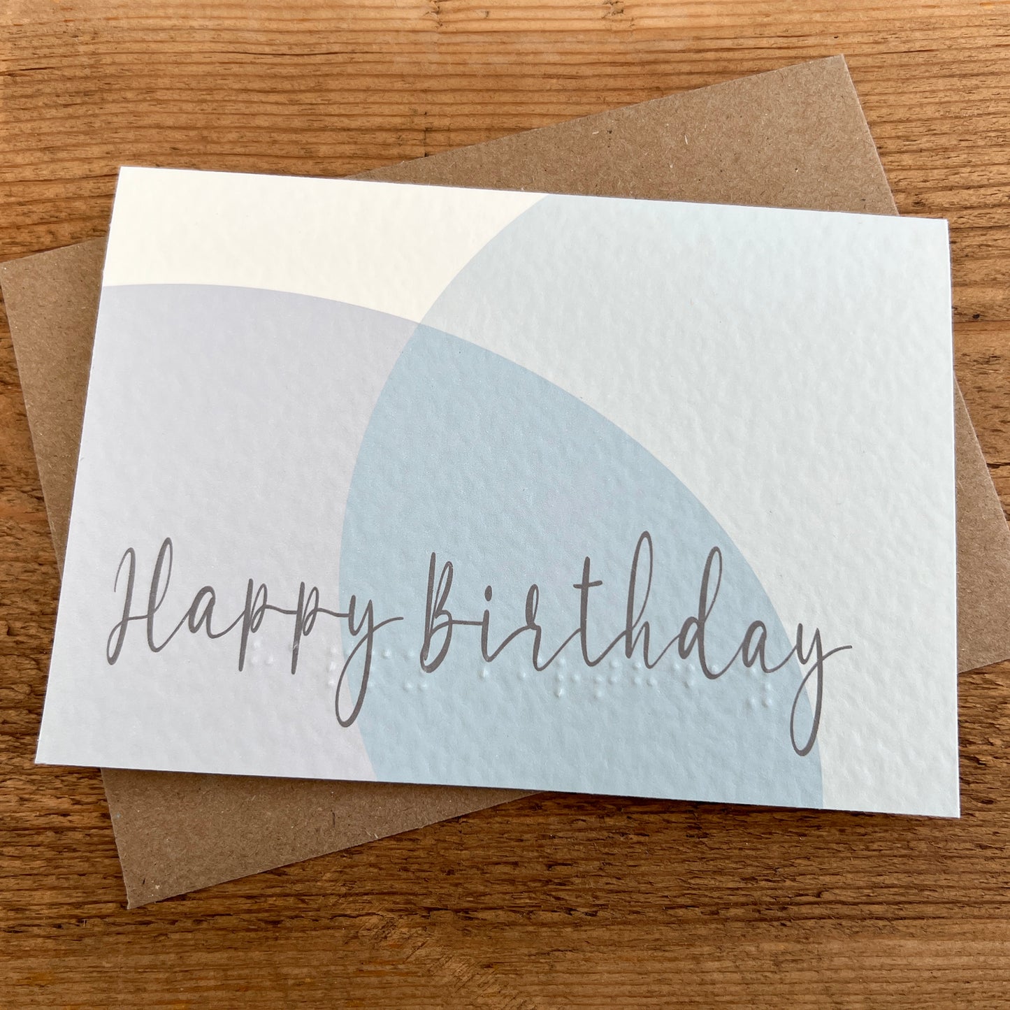 Birthday card with 'Happy Birthday' text and abstract pastel circles, featuring Braille underneath.