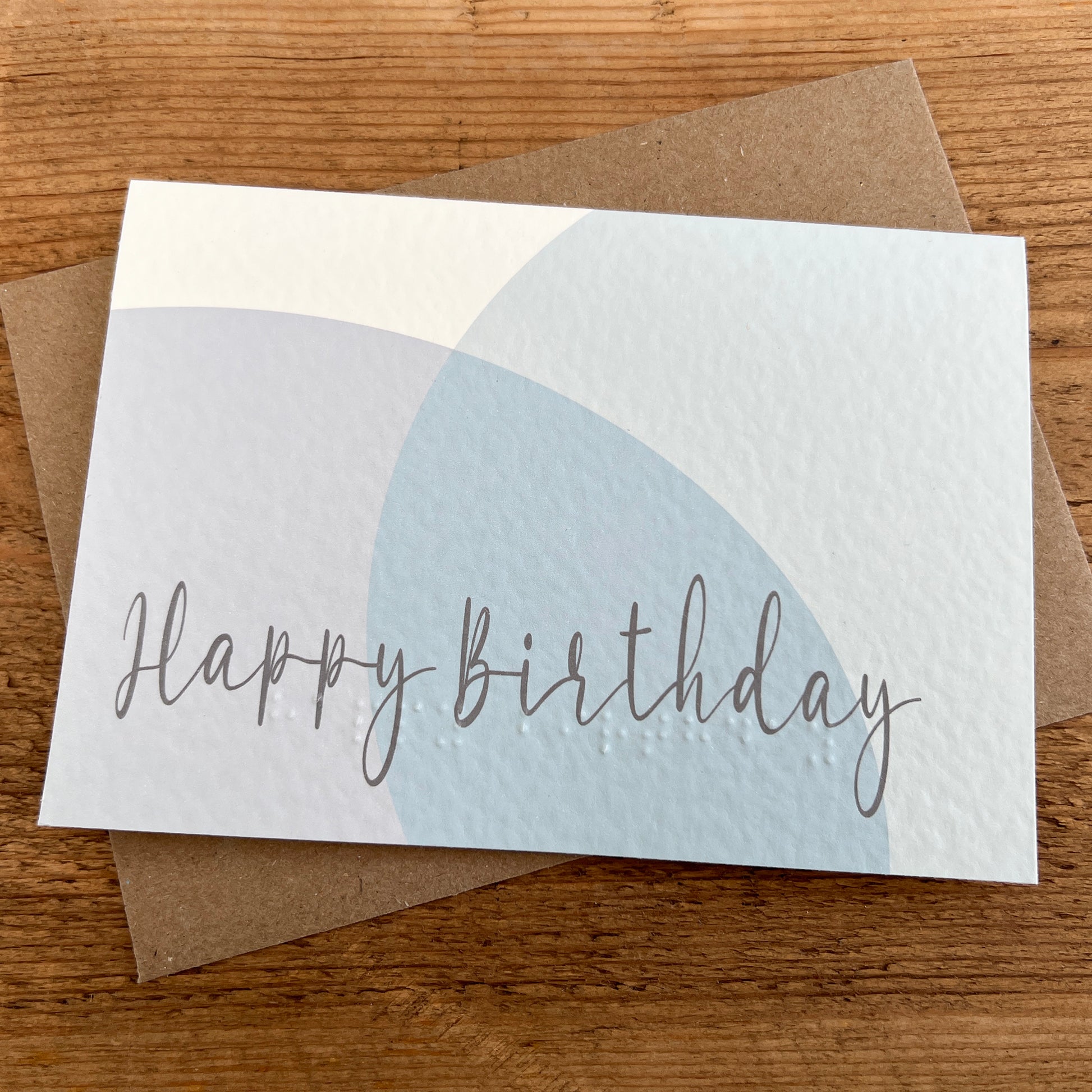 Birthday card with 'Happy Birthday' text and abstract pastel circles, featuring Braille underneath.