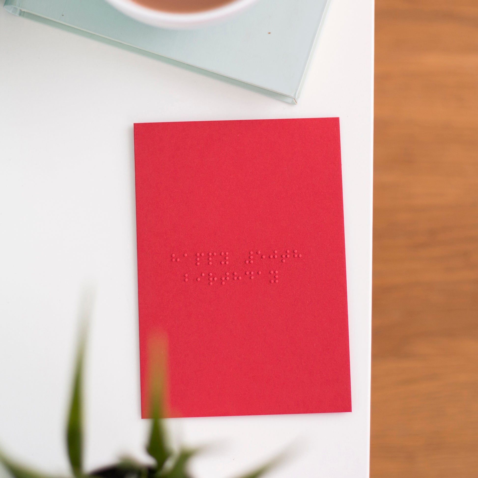 A vibrant red card lay flat on a table with happy 50th birthday written in lower case grade one braille. 