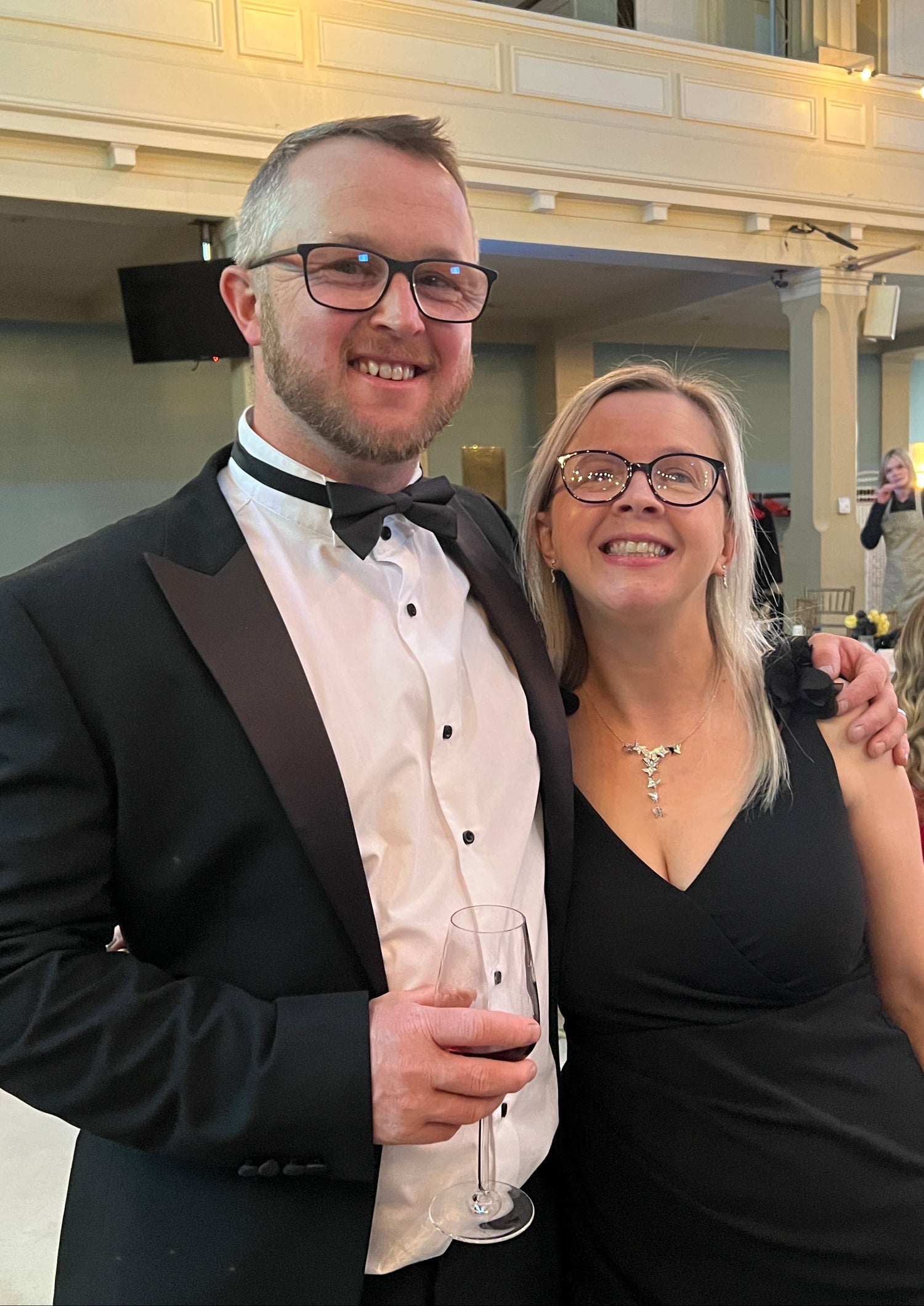 Hayley and her husband Scott at the Small Awards, both are wearing black tie, Scott is holding a glass of wine.