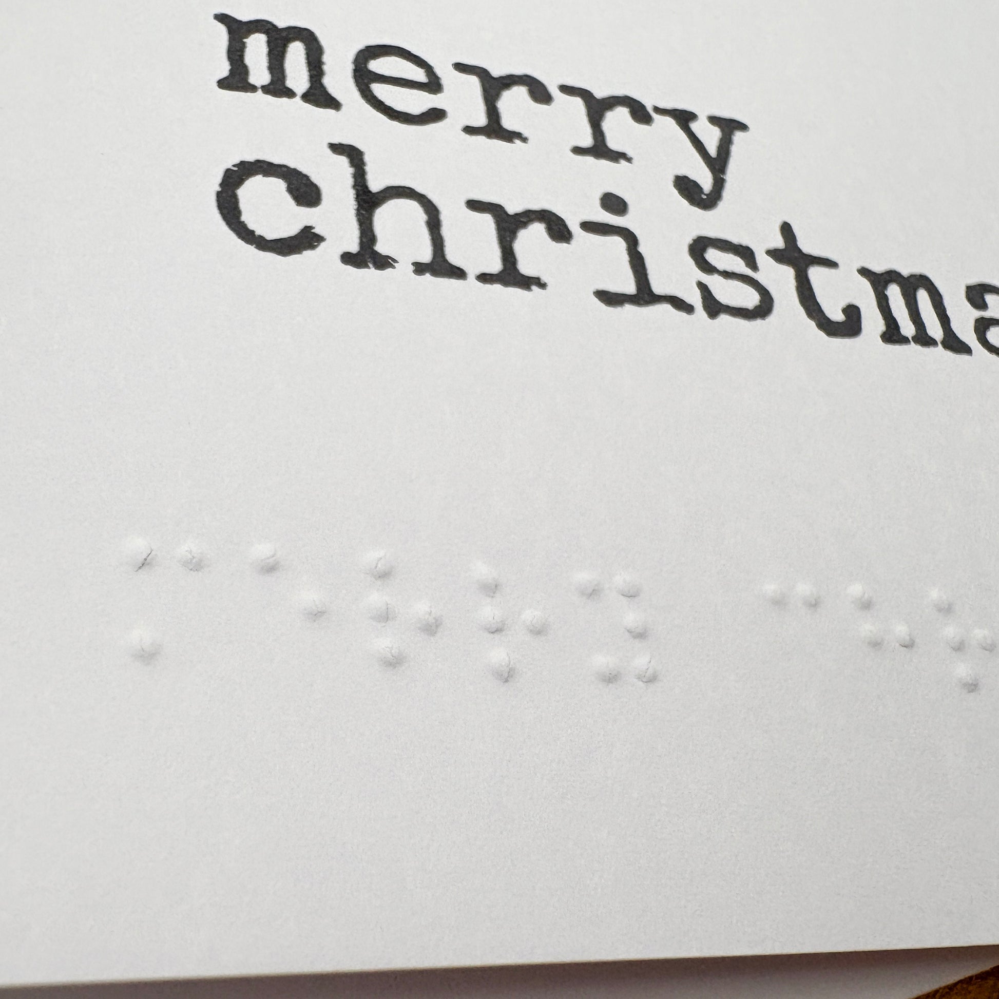 A close up of a white A6 card with Merry Christmas written in black typewriter style font and the same in braille beneath the printed text.