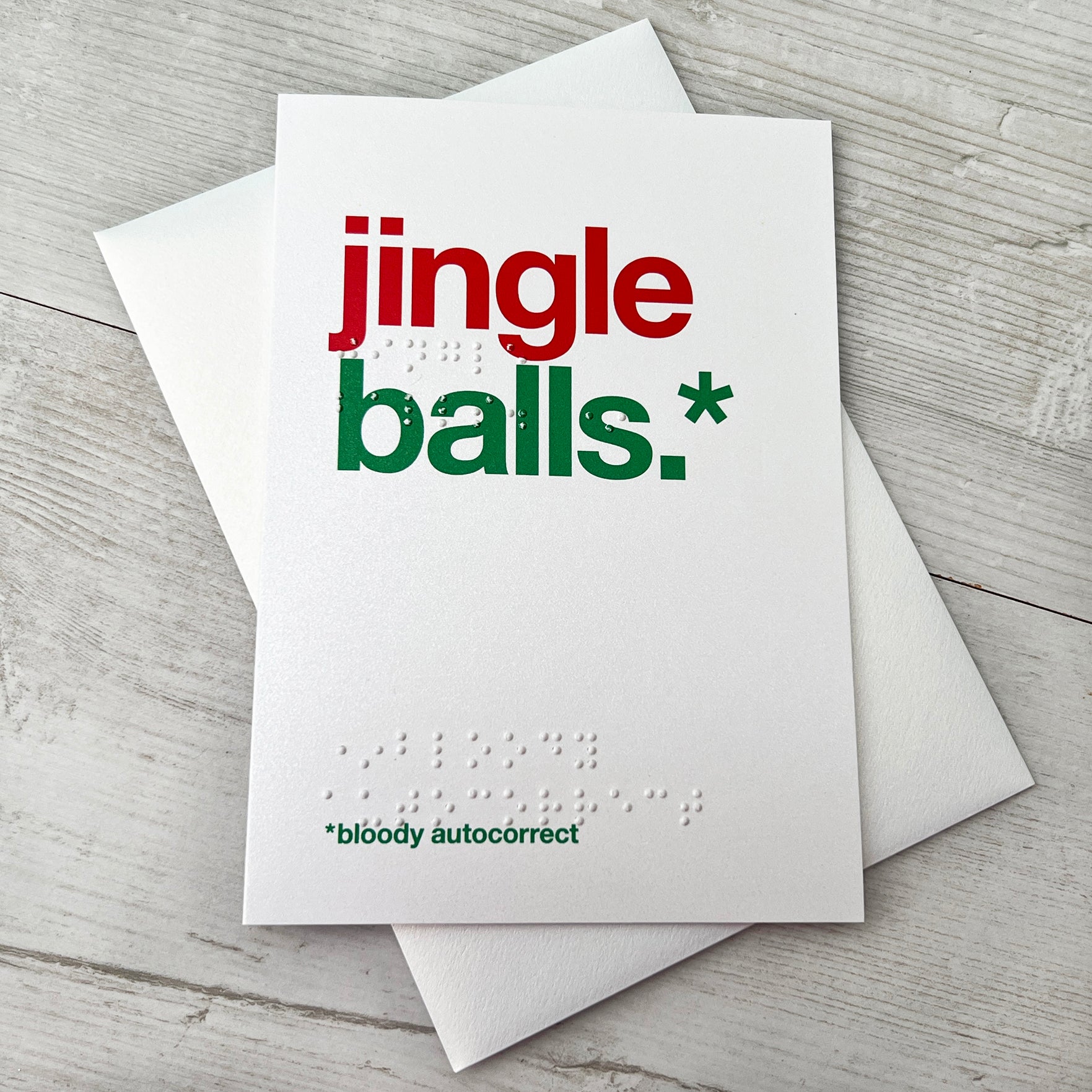 A white card with colourful text saying jingle balls.* *bloody autocorrect with braille saying the same.