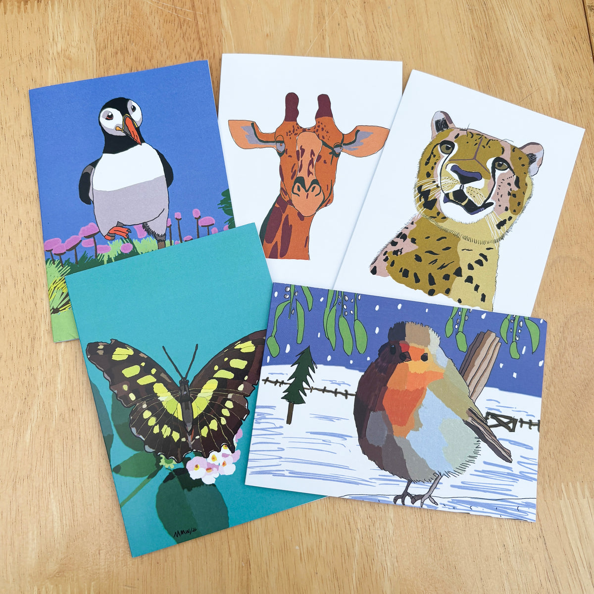 A collection of illustrated greetings cards showing a puffin, a giraffe, a cheetah, a butterfly and a robin. 