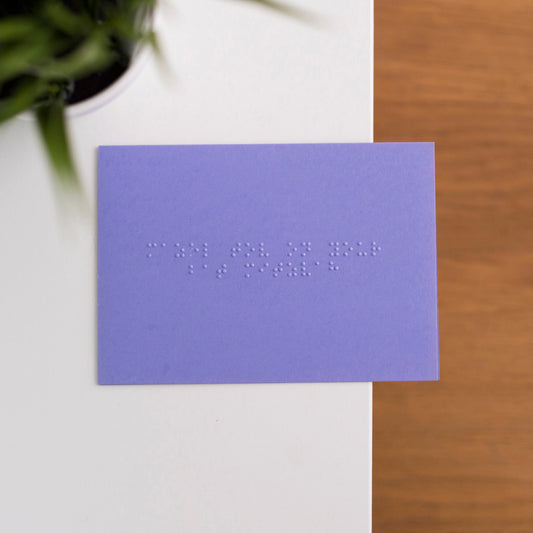 A vibrant purple card lay flat on a table with mazel tov on your bat mitzvah written in lower case grade one braille. 