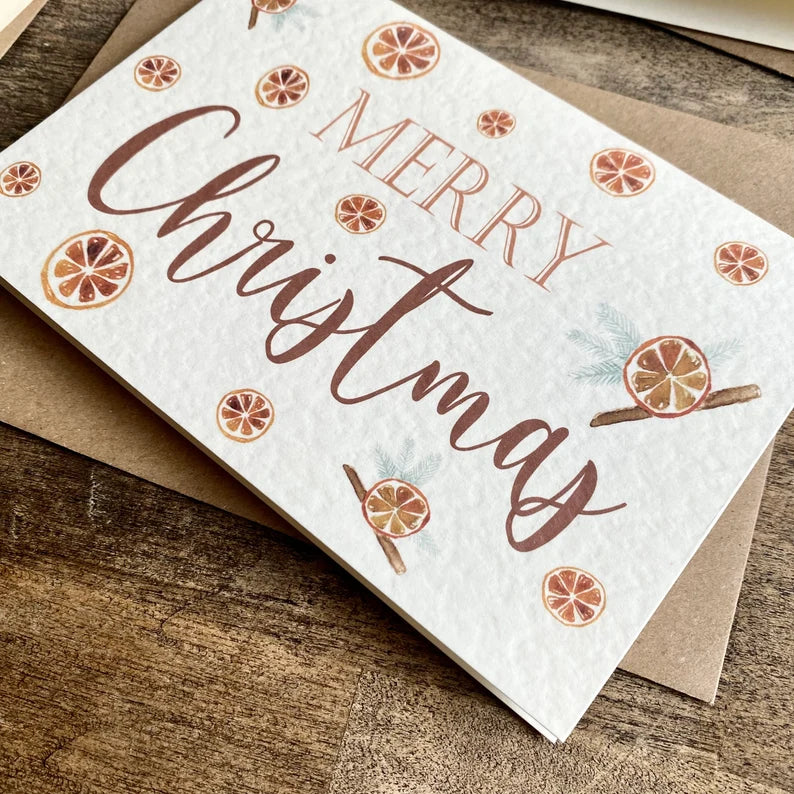 A textured white card with Merry Christmas written in a red font with citrus drawings around the card.