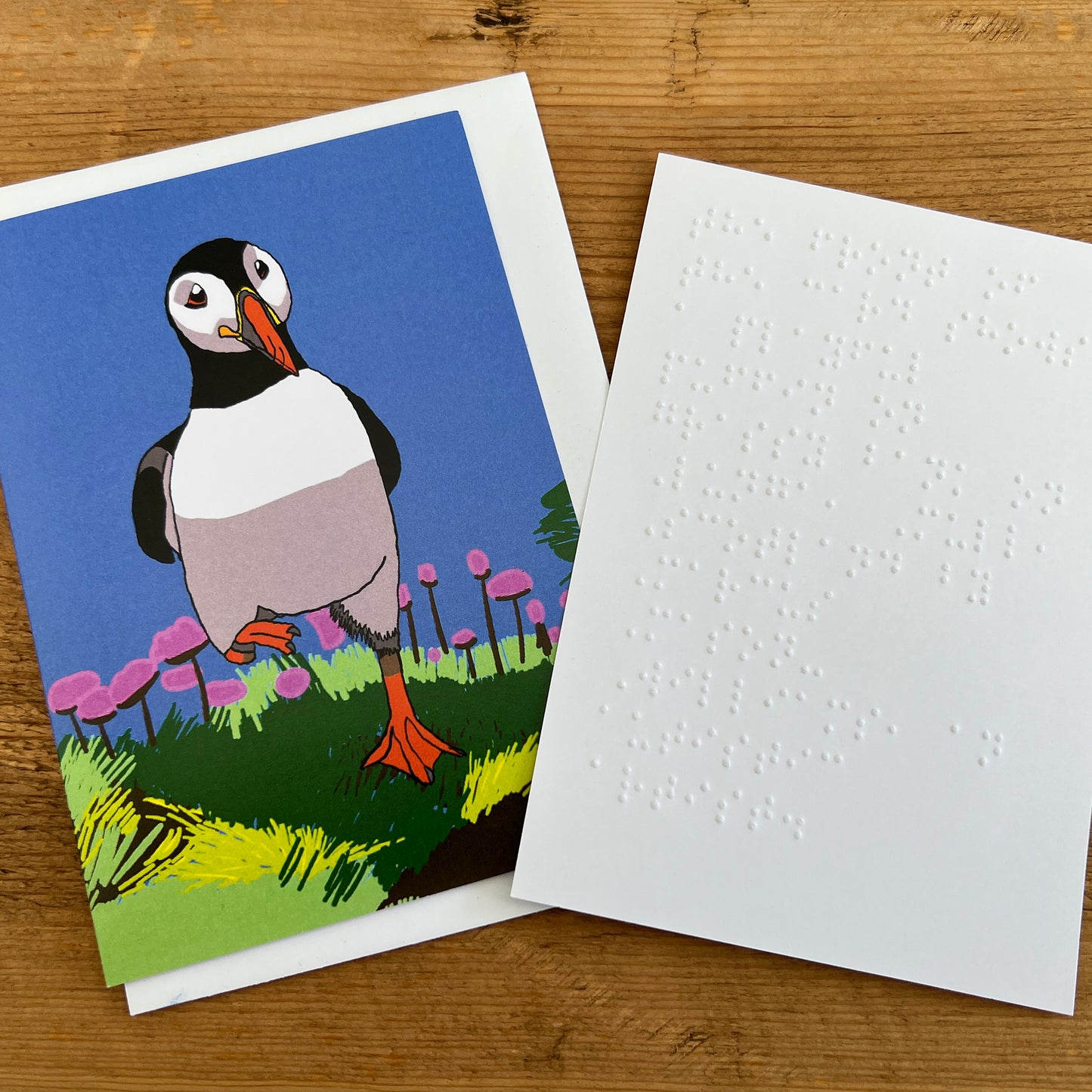 Greetings card showing a puffin walking in a meadow with a separate white insert embossed with Braille.