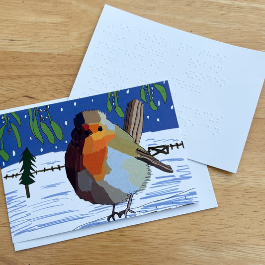 A greetings card showing a colourful illustration of a robin perched on a wooden fence in a snowy winter scene.. There is a white braille note at the side.