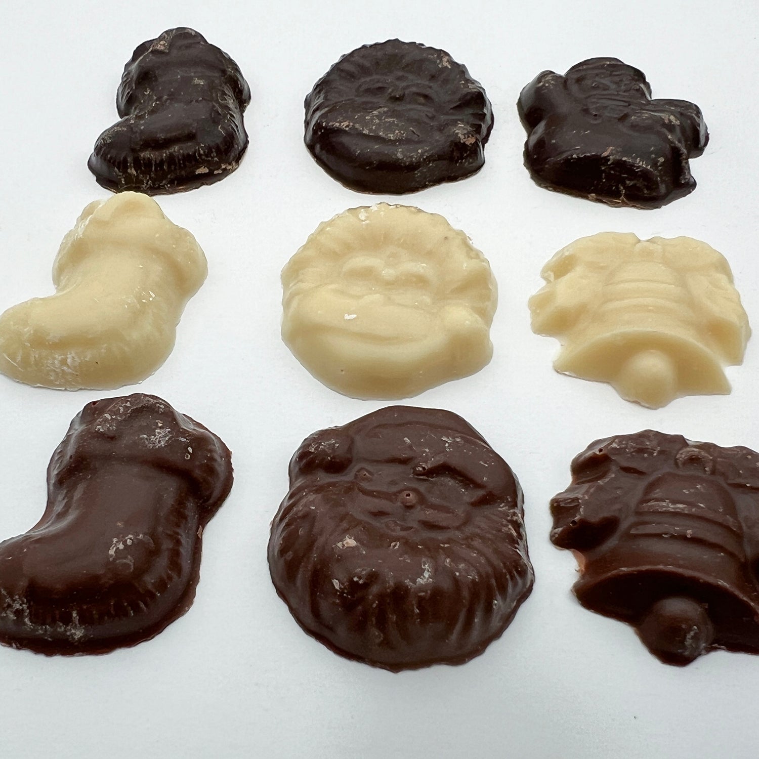 A close up of nine pieces of chocolate in various Christmas themed shapes such as a bell, santa and a stocking. The chocolate is a mix of white, dark and milk.