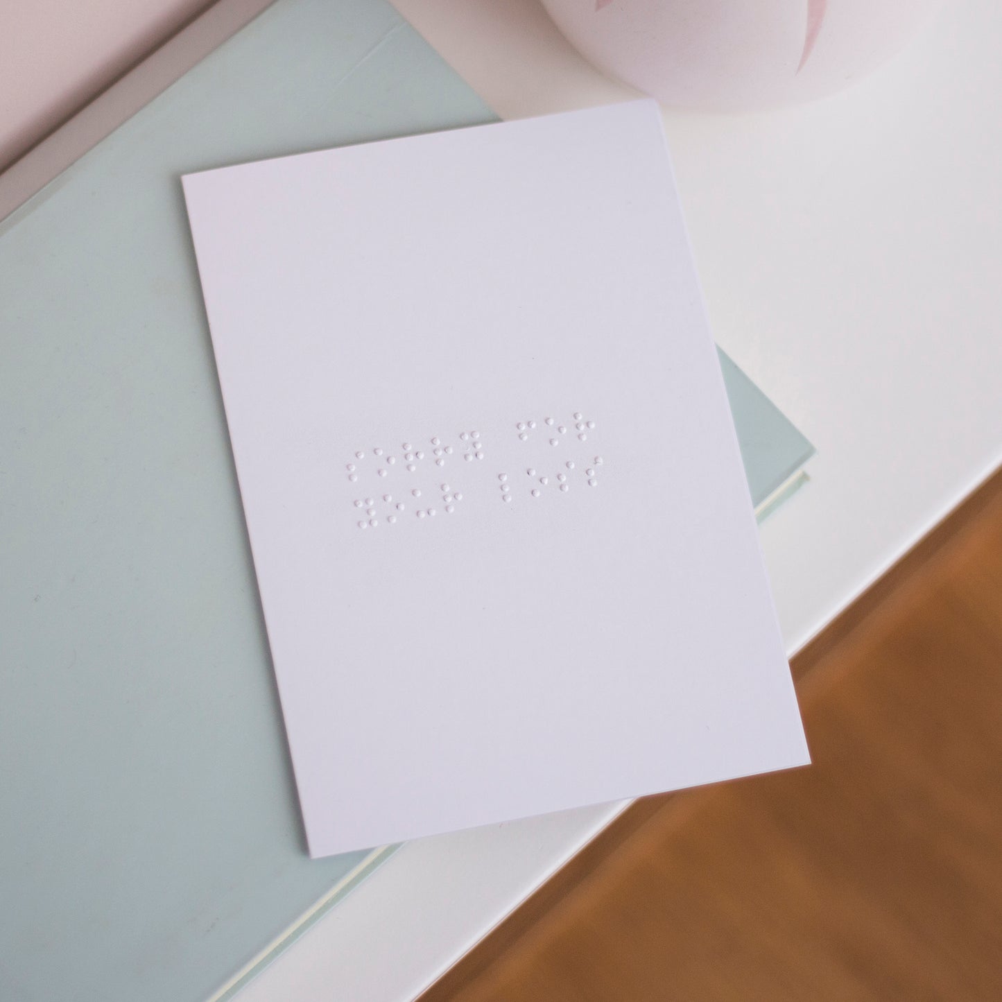 An A6 white card, lay flat on a table with "sorry for your loss" written in braille.