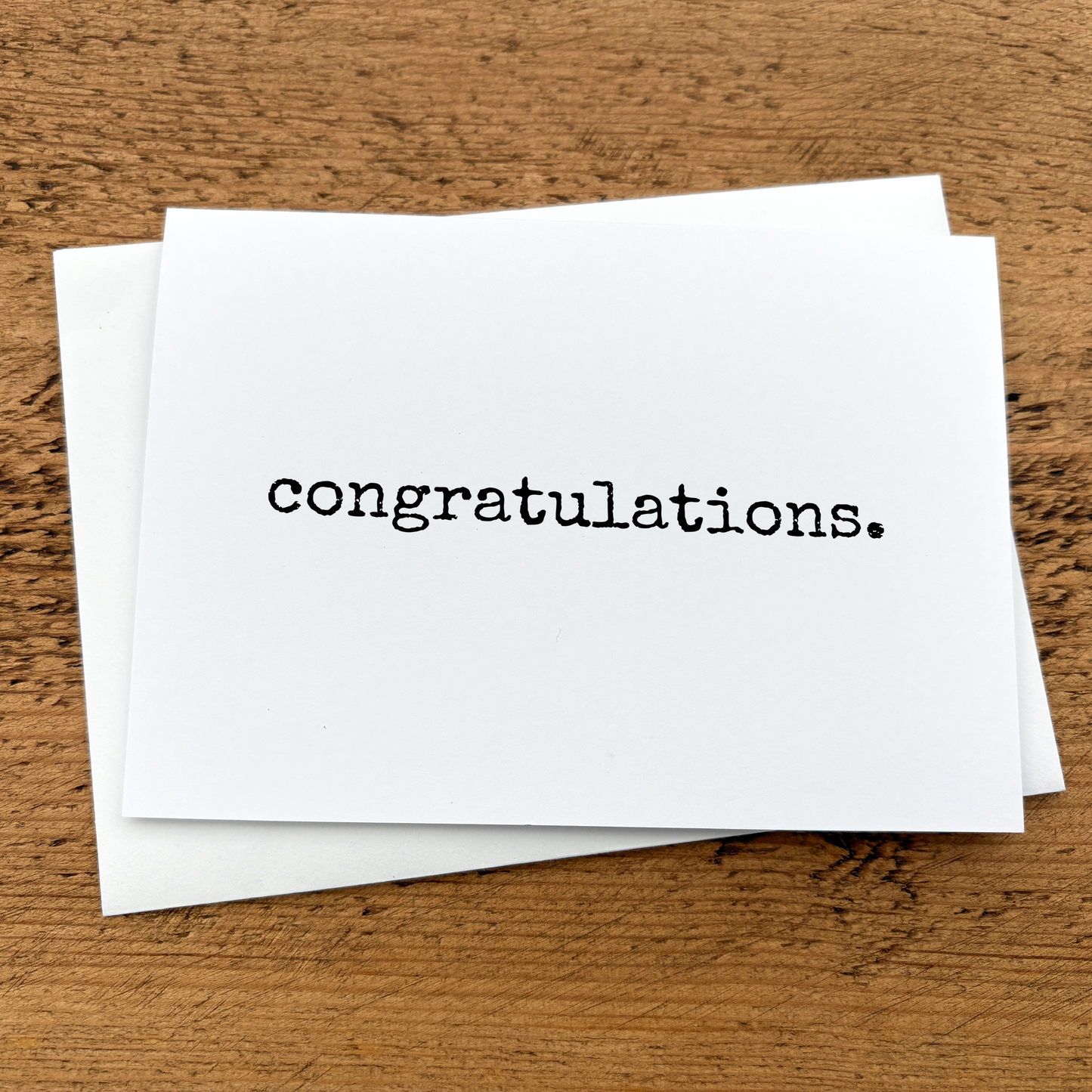A white A6 card with text that reads: congratulations written in black typewriter style font.