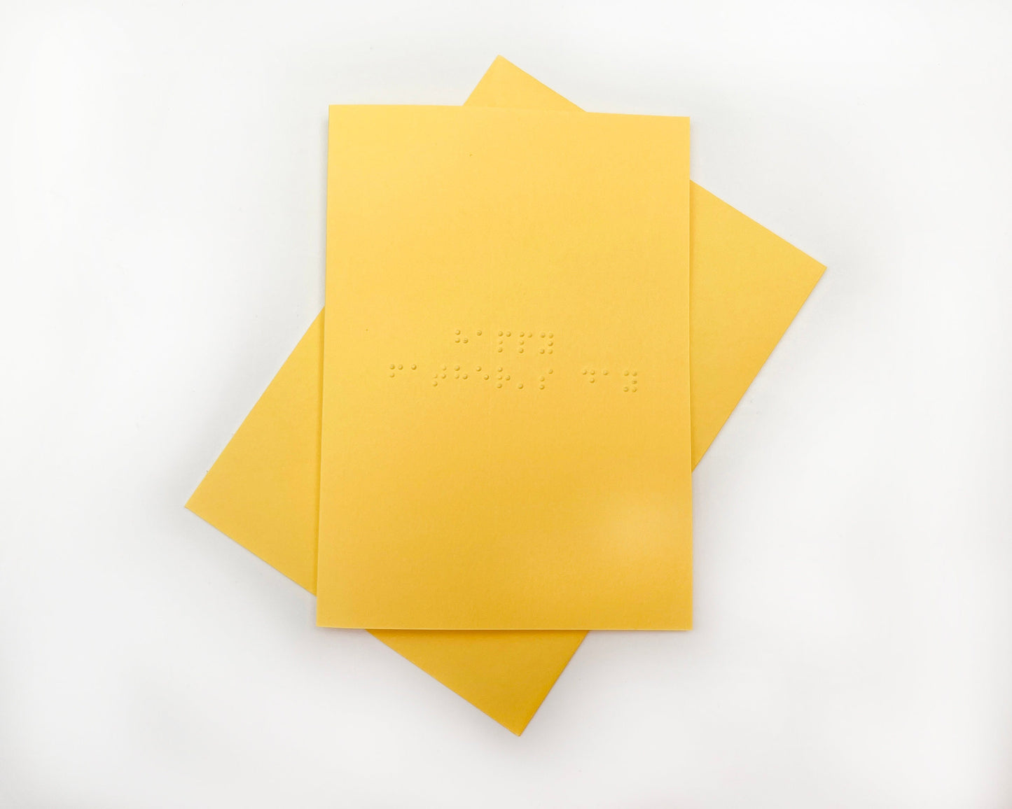 Image shows a yellow card with the words happy father&#39;s day written in grade 1 UEB braille. A matching yellow envelope is beneath the card.
