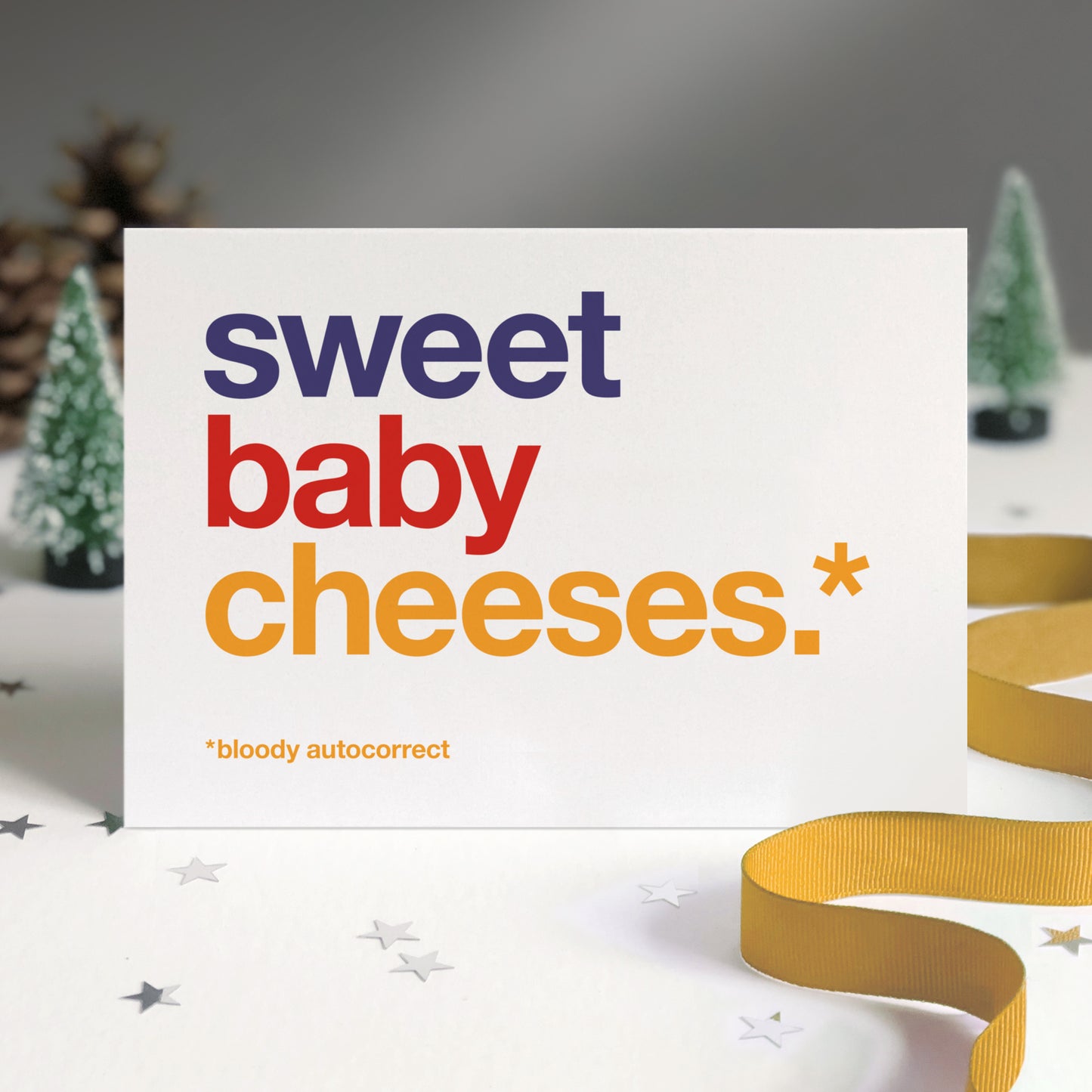 A white card with colourful text saying sweet baby cheeses.* *bloody autocorrect