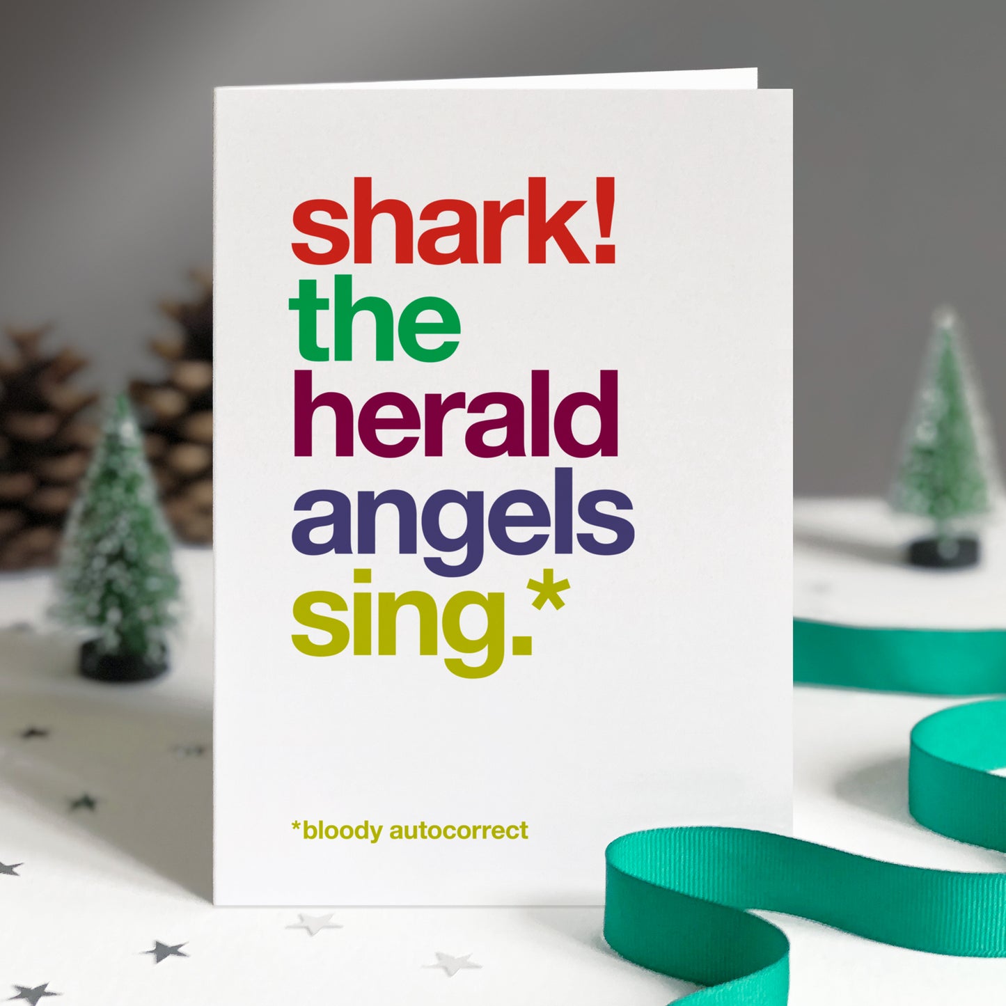 A white card with colourful text saying shark! the herald angels sing.* *bloody autocorrect