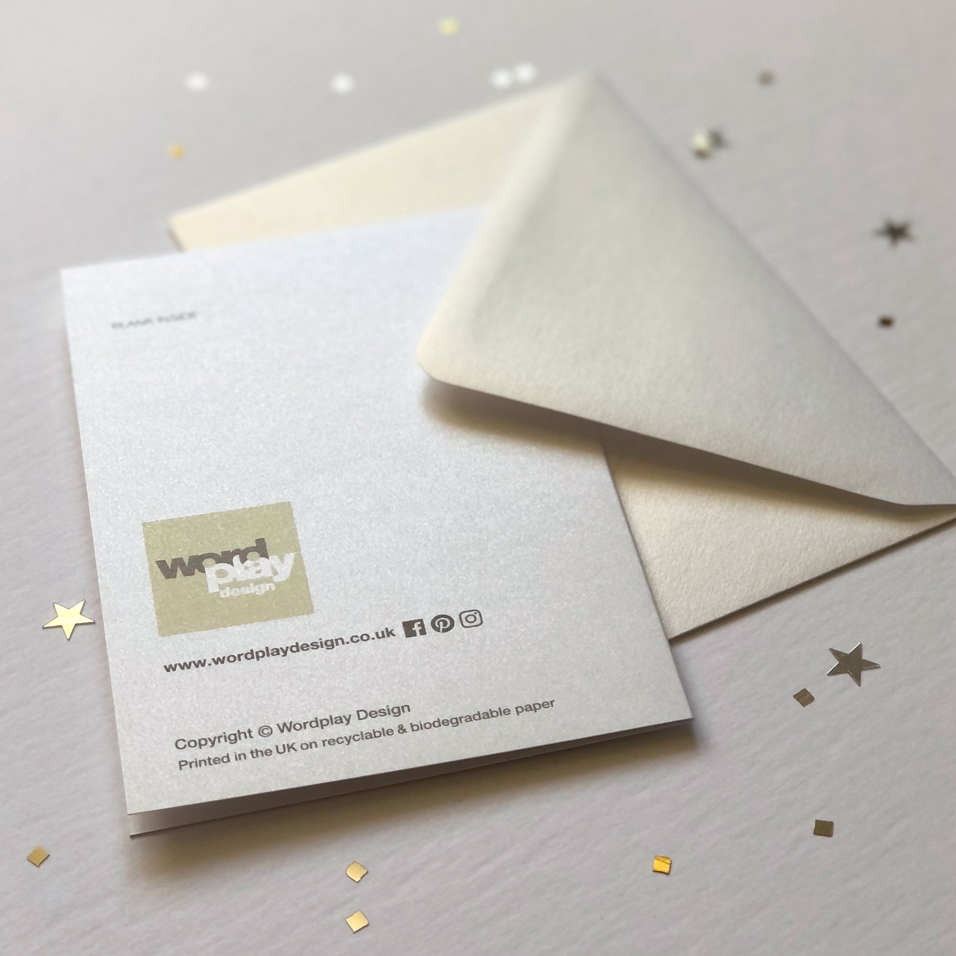A pearlescent envelope and a greeting card facing down showing the Wordplay Design logo.