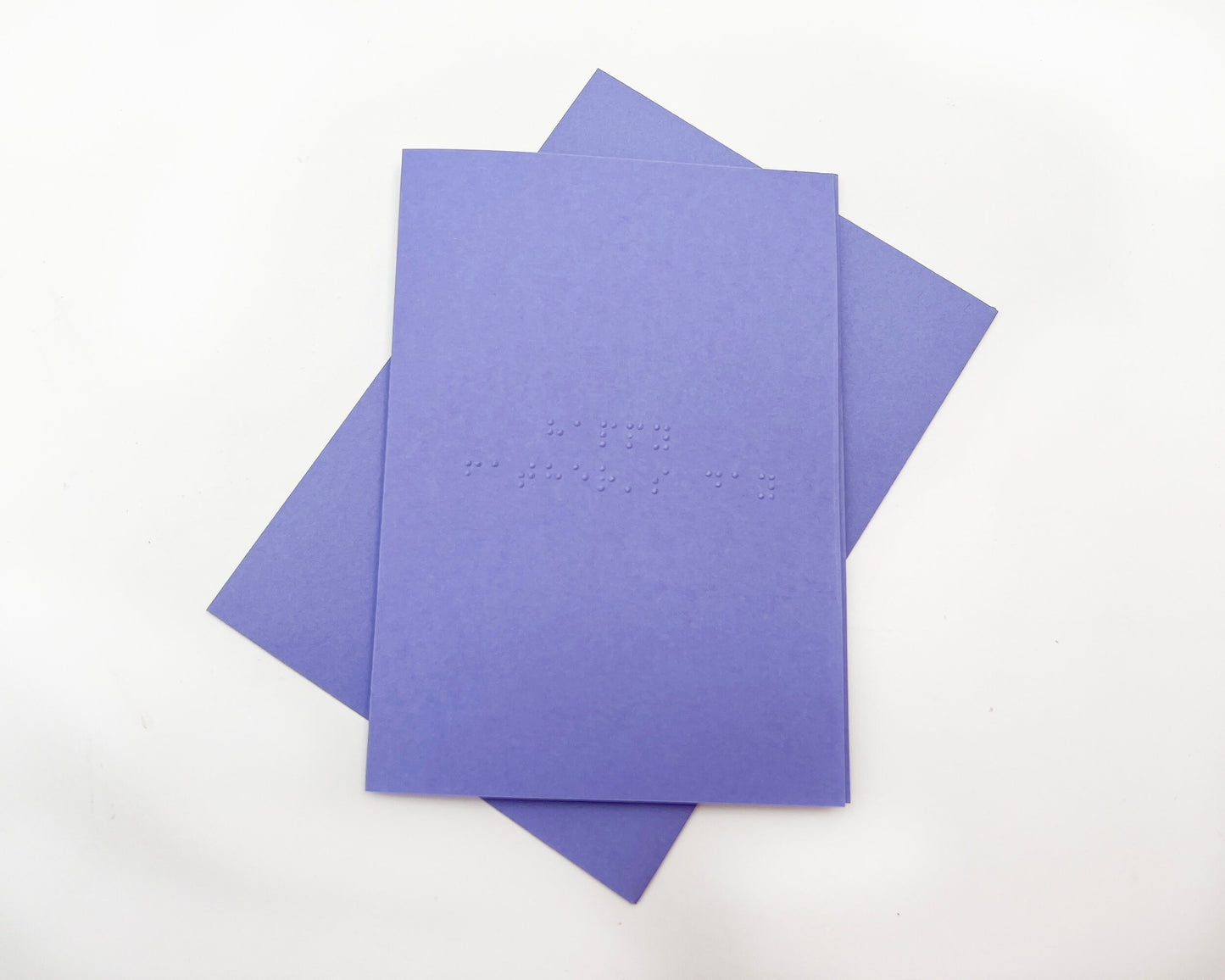 Image shows a purple card with the words happy father&#39;s day written in grade 1 UEB braille. A matching purple envelope is beneath the card.