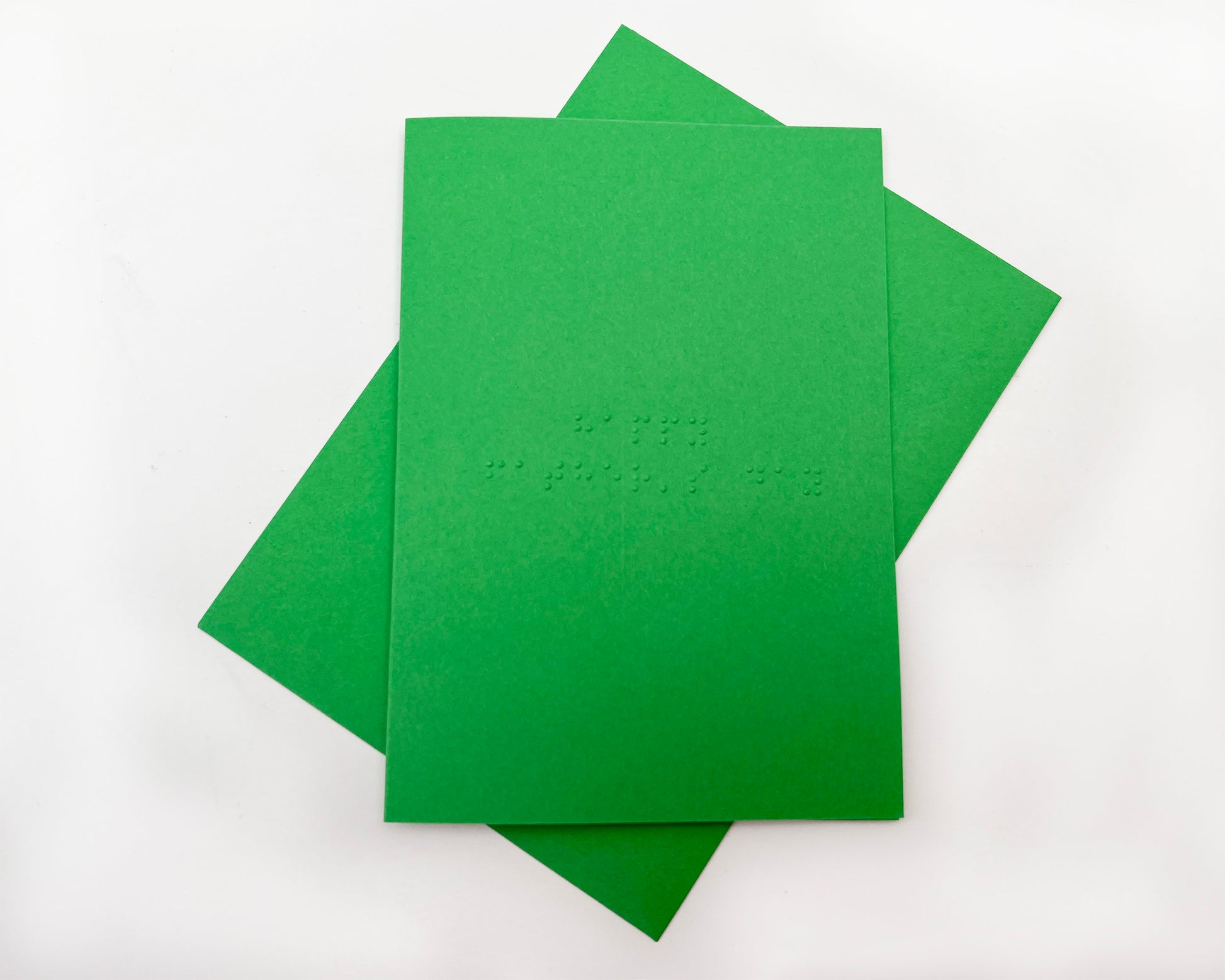 Image shows a green card with the words happy father&#39;s day written in grade 1 UEB braille. A matching green envelope is beneath the card.