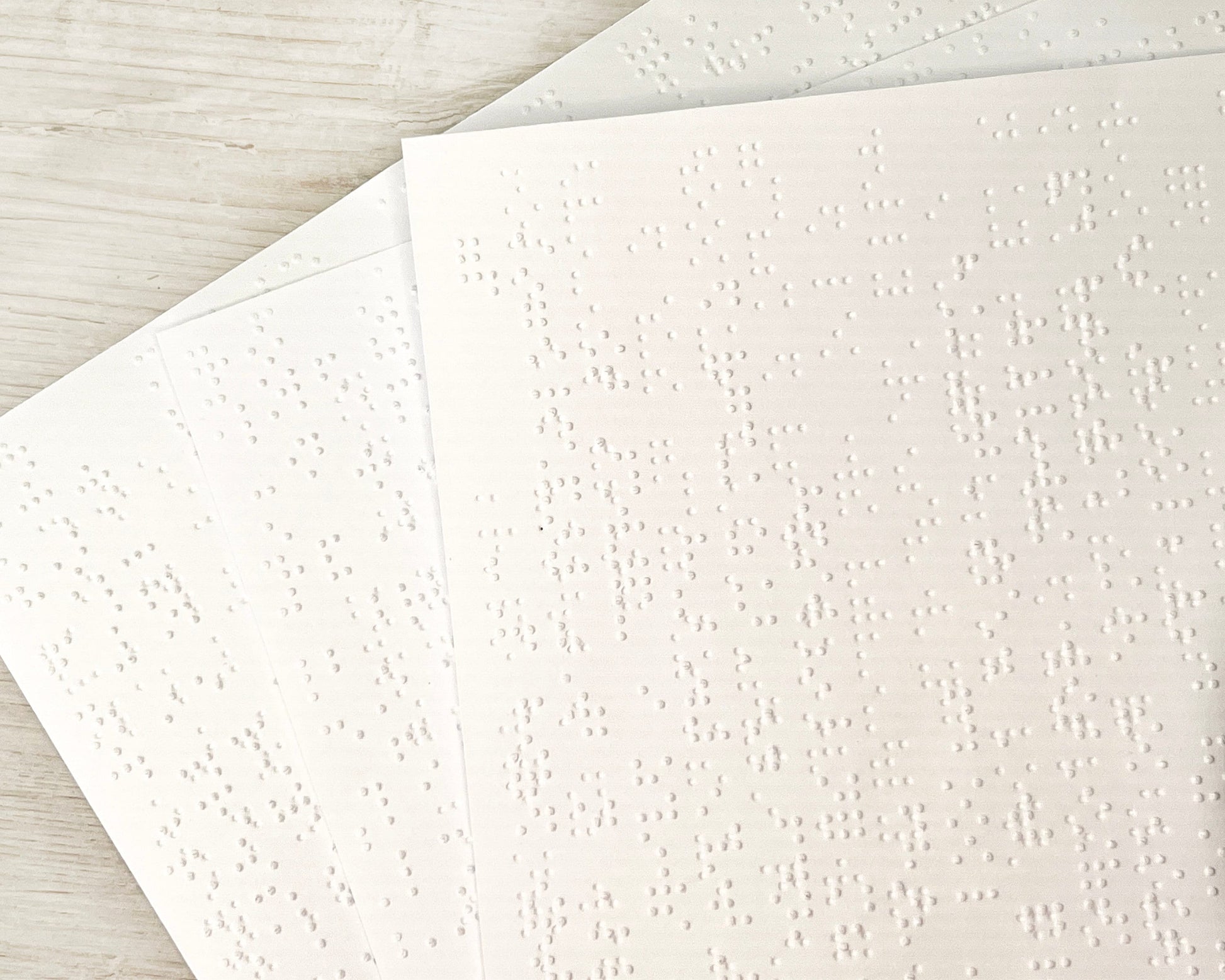 A close up of three sheets of 22x23cm white braille paper.