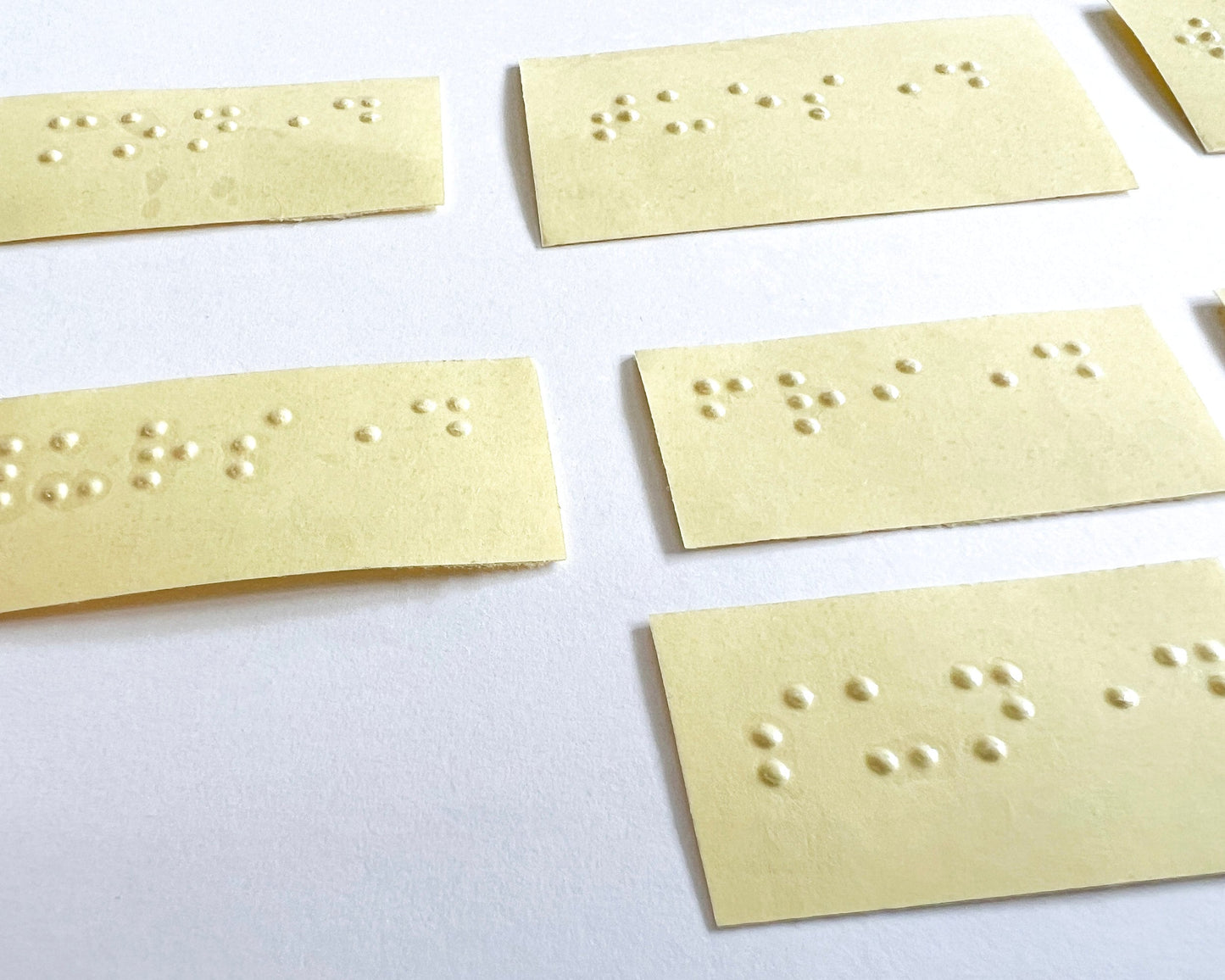 A close up of some of the days of the week braille labels. Labels are on a yellow backing paper and the labels themselves are clear.