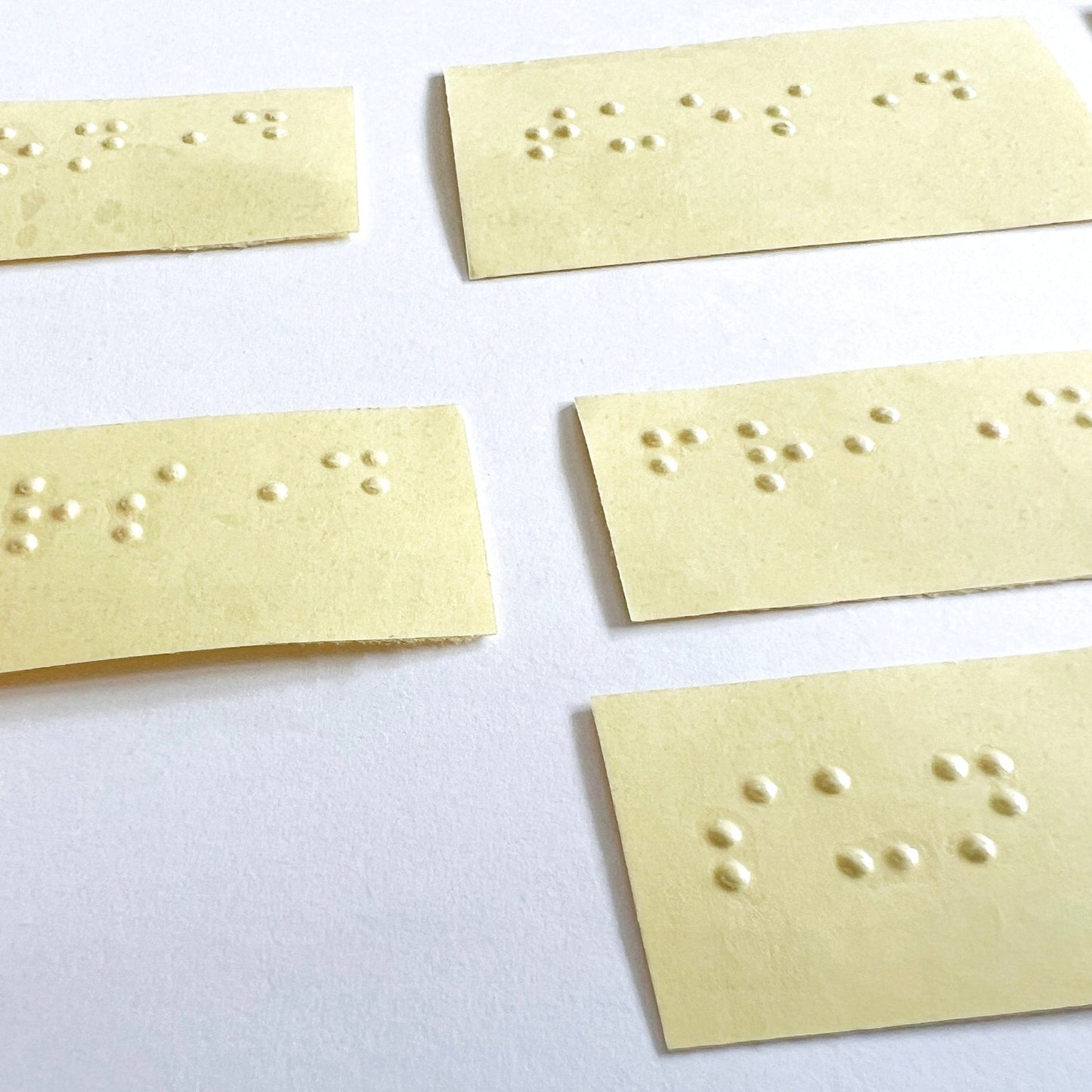 A close up of some of the days of the week braille labels. Labels are on a yellow backing paper and the labels themselves are clear.