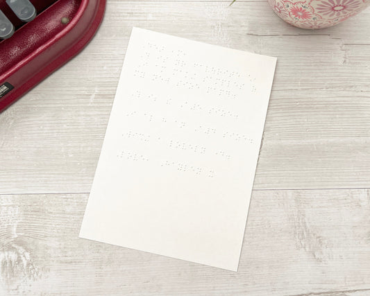 An A5 piece of white braille paper with a Perkins brailler to the left and a plant pot on the right.