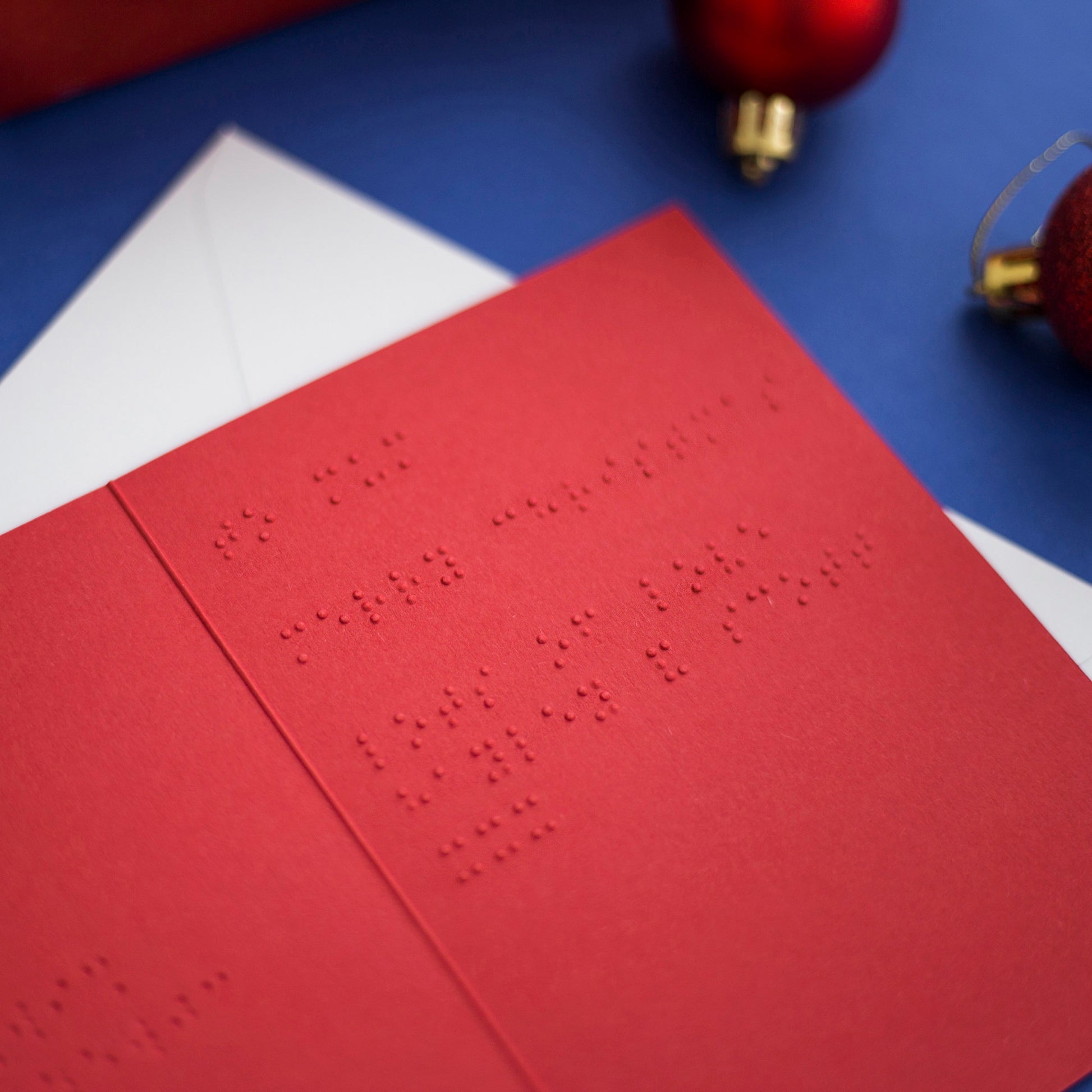 An open red Christmas card with braille inside, lay on a white envelope