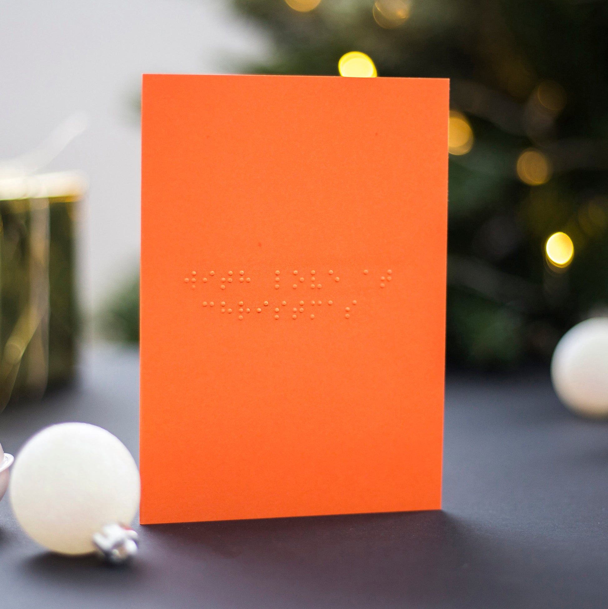 An orange braille Christmas card saying With Love at Christmas written in lower case UEB.